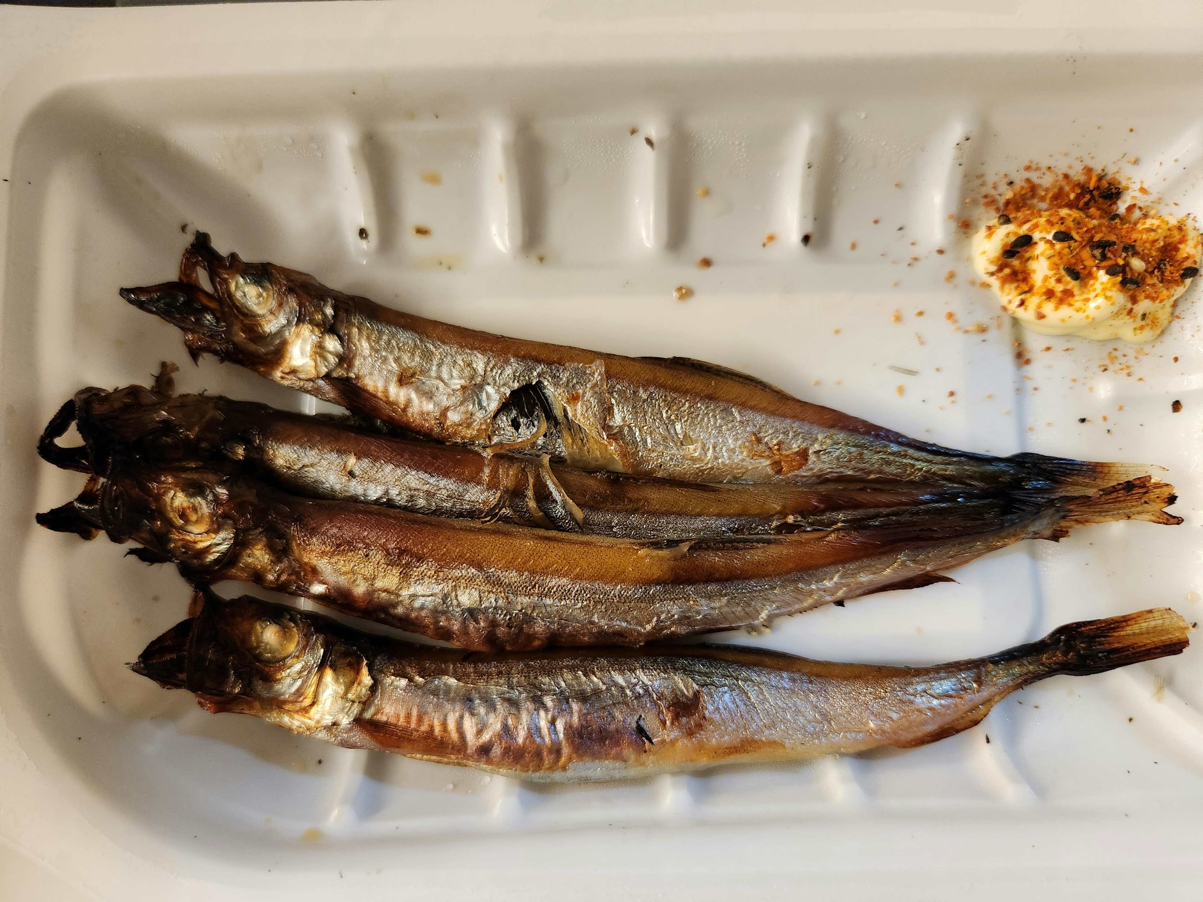 Grilled fish arranged on a white plate with a condiment on the side