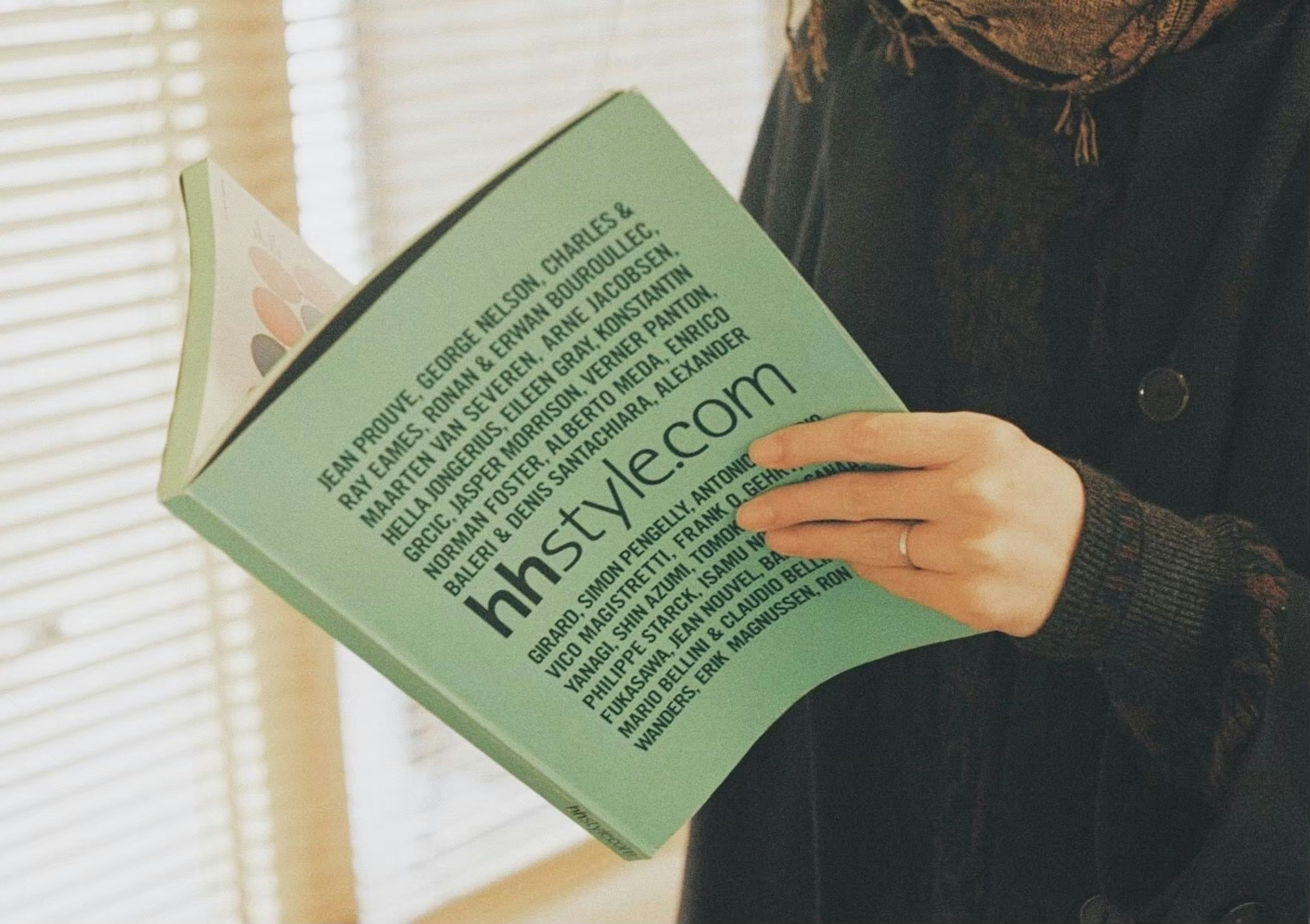 A woman holding a green magazine with natural light coming through a window