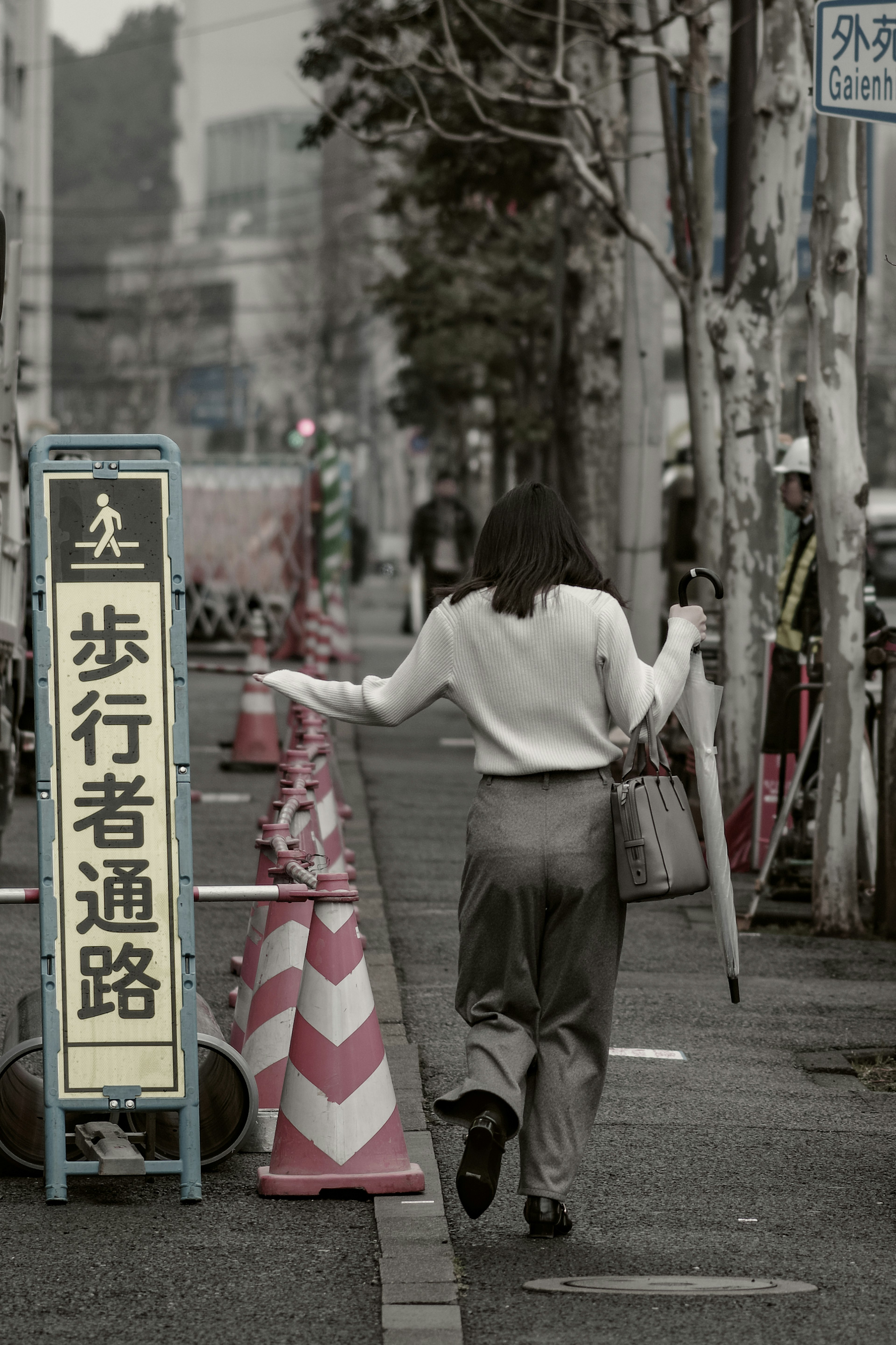 A woman walking with an umbrella near a pedestrian sign