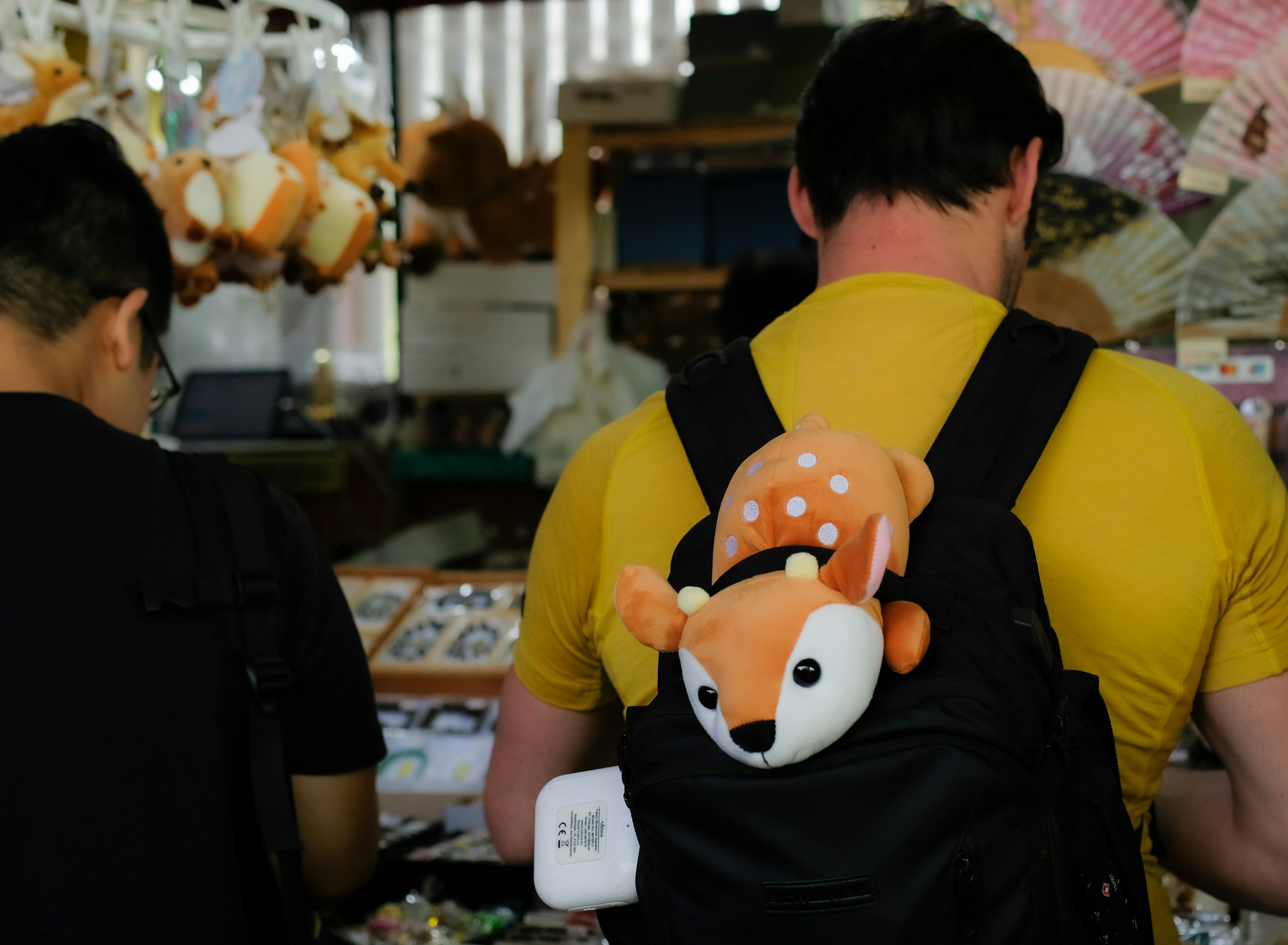 A man with a fox plush toy on his backpack in a shop filled with various items