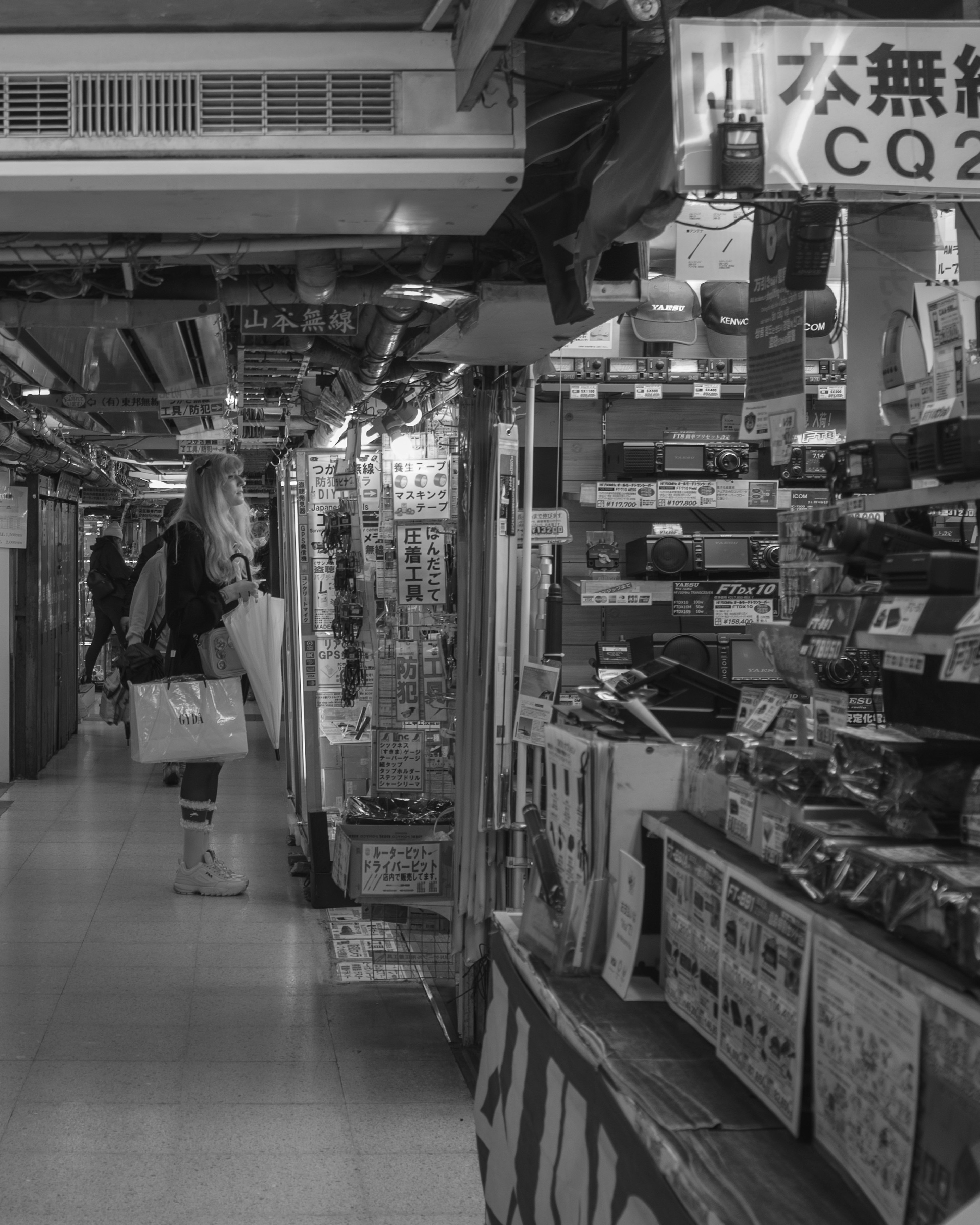 Une femme se tenant dans une arcade commerçante en noir et blanc avec des magasins exposant divers produits