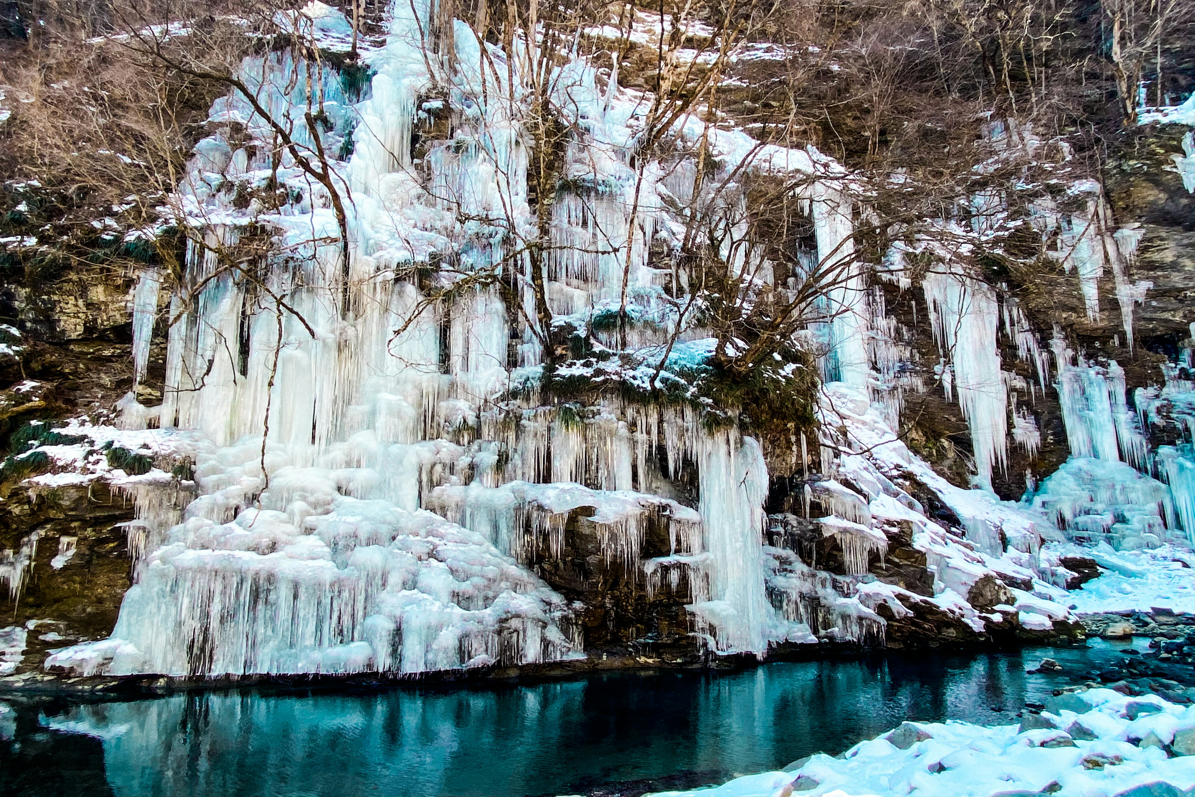 Frozen cliffside with cascading ice and a turquoise stream