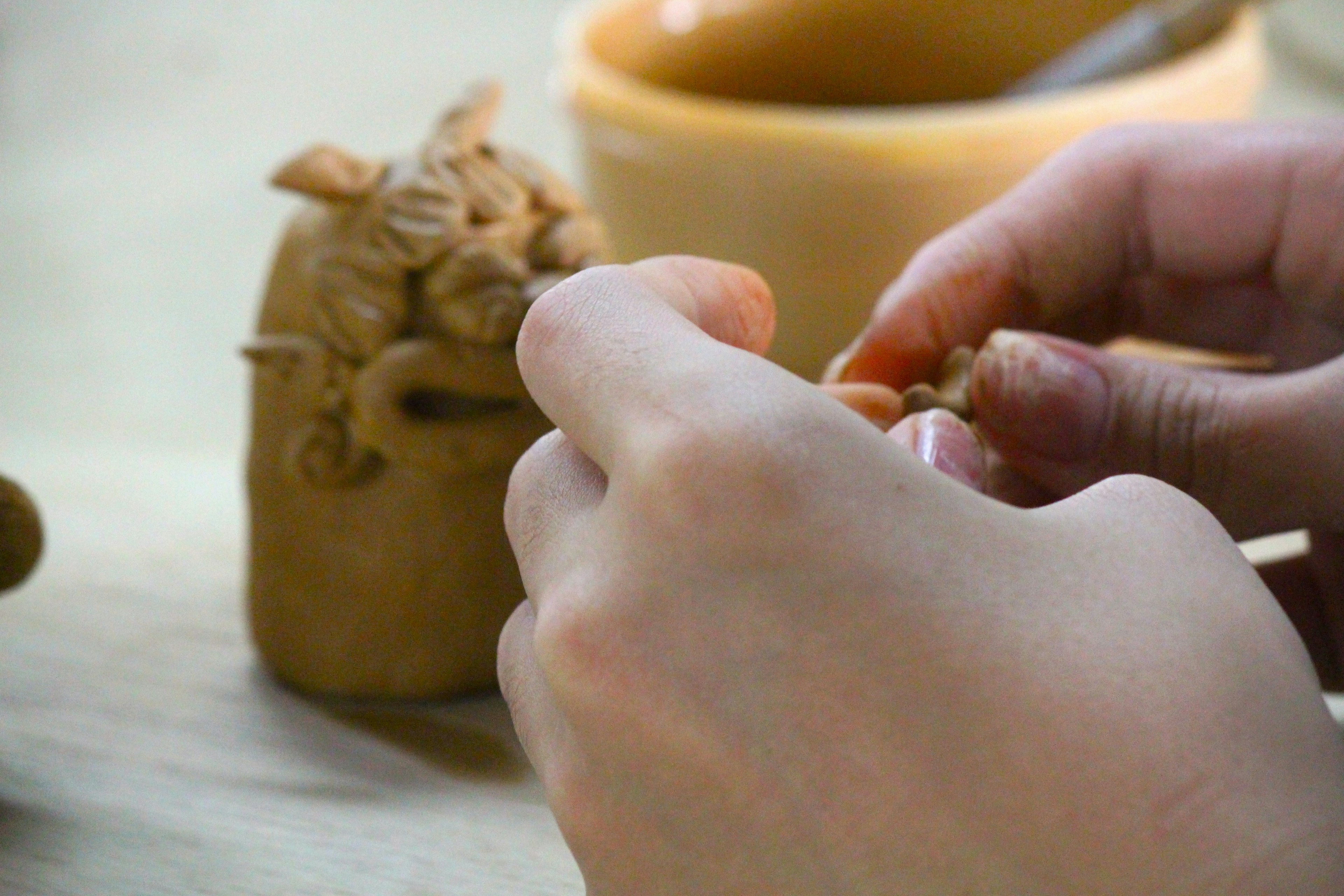 Hands sculpting clay with a small clay figure and a bowl in the background