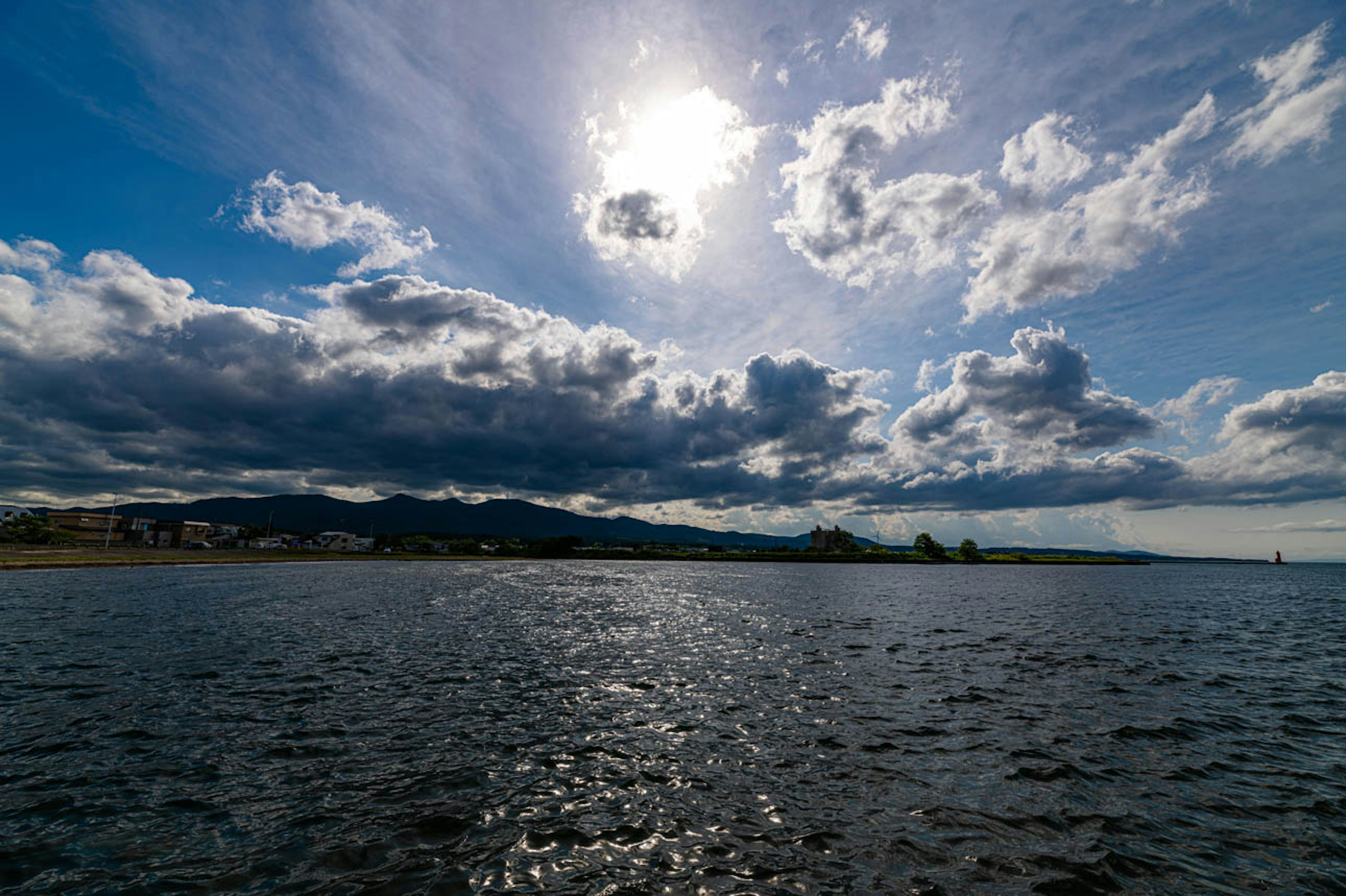 Vista panoramica di un cielo blu con nuvole e un sole che si riflette sulla superficie dell'acqua