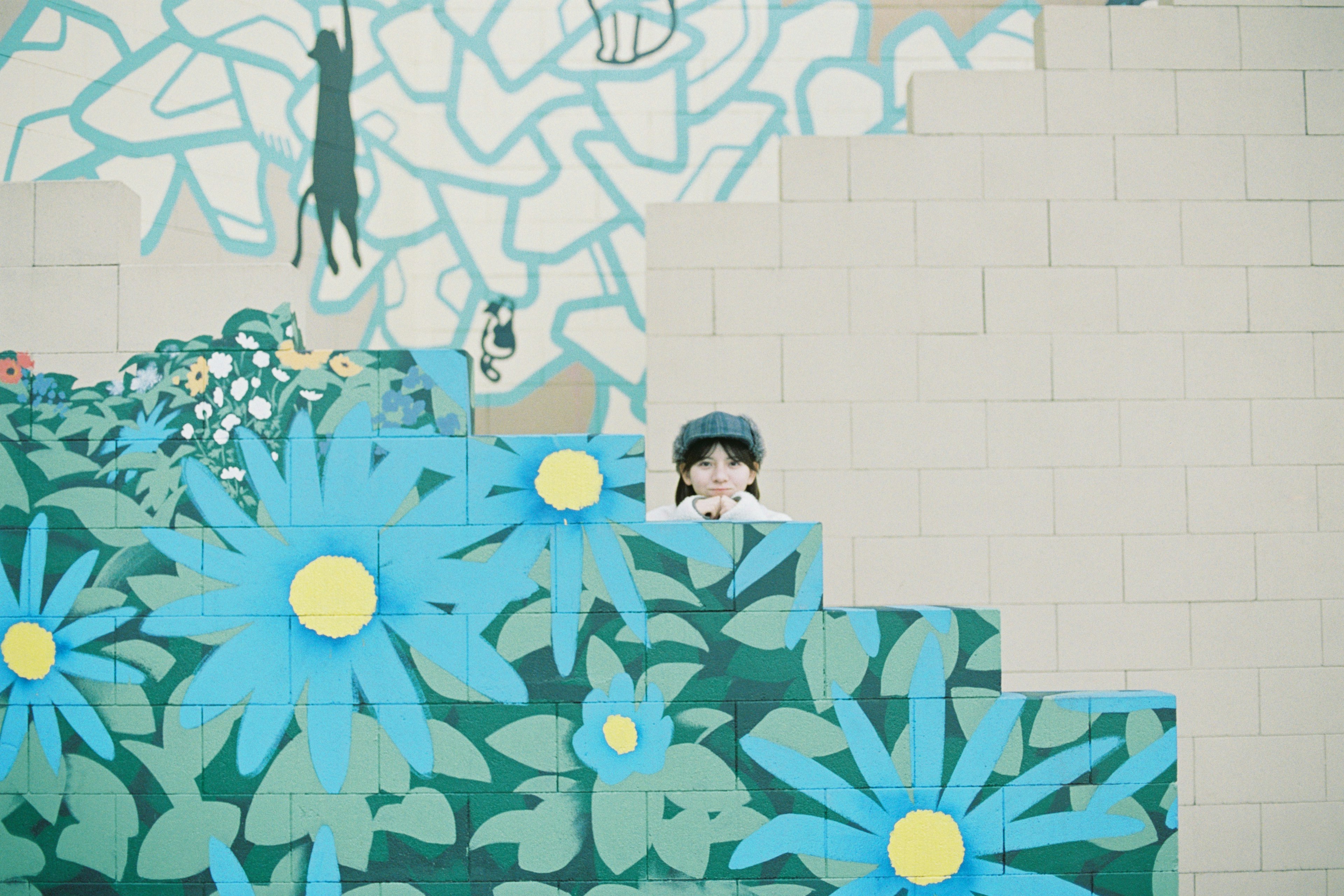 Child peeking from behind vibrant blue flower mural