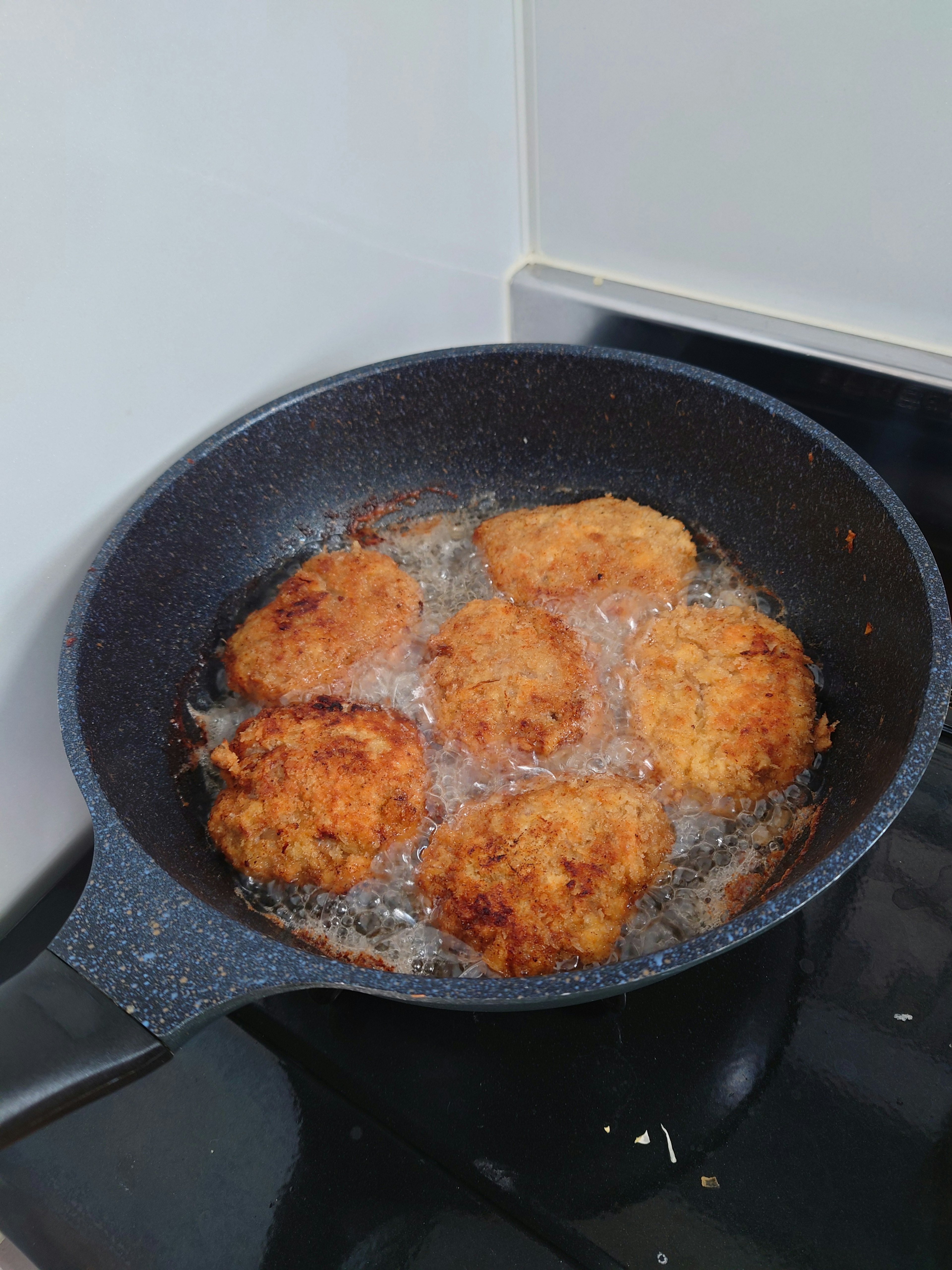 Seis croquetas doradas friendo en una sartén