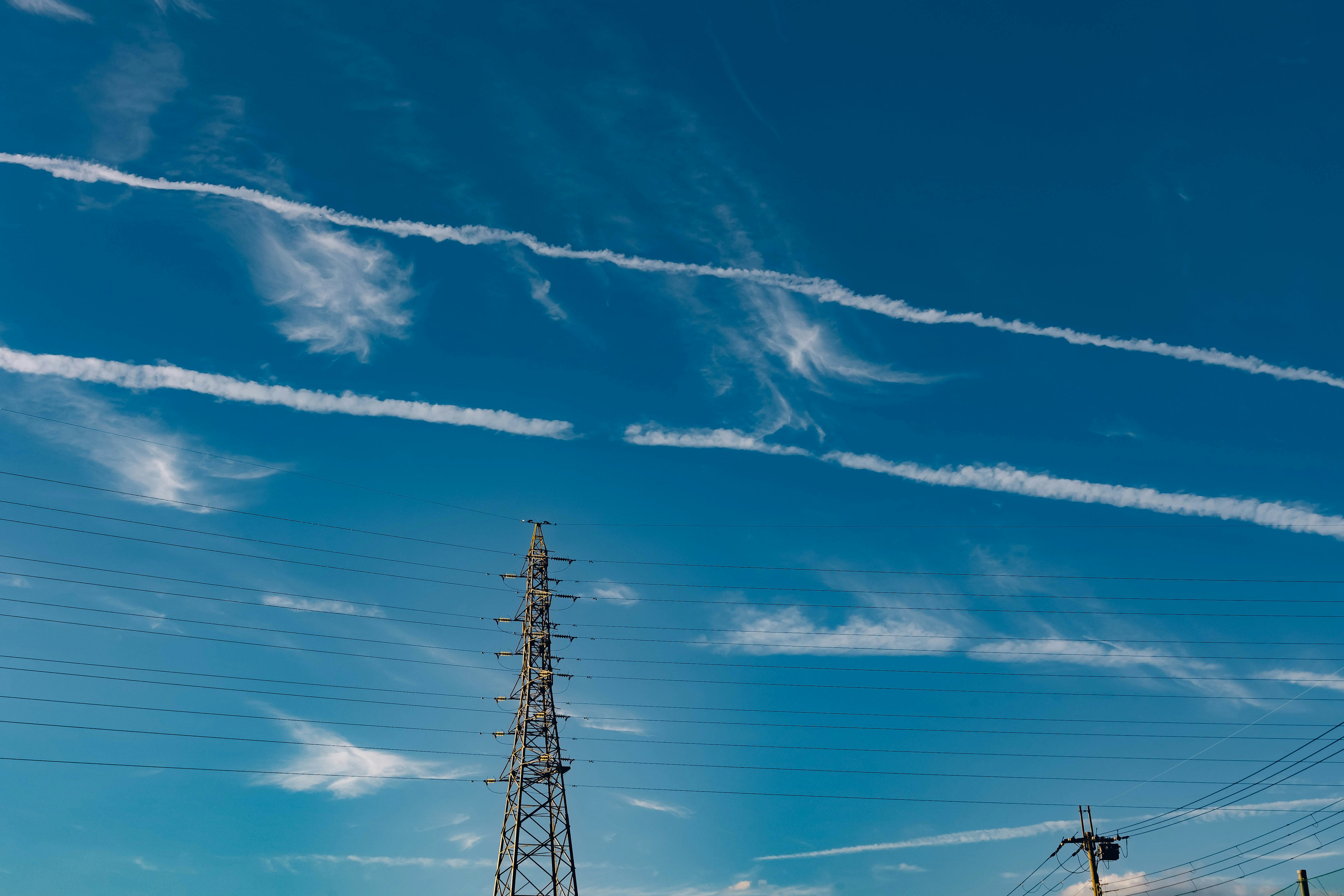 Blauer Himmel mit weißen Kondensstreifen und einem Funkmast