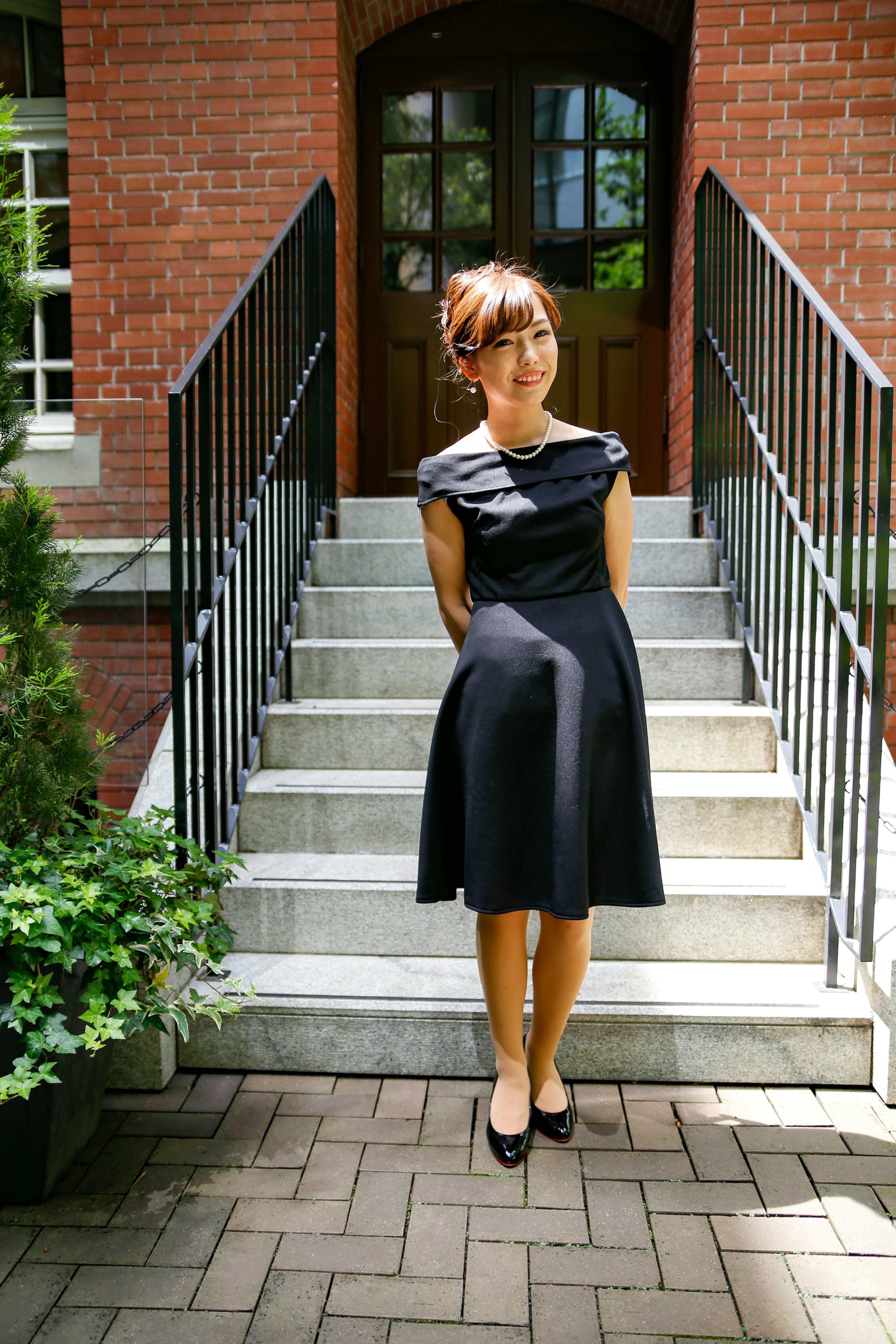 A woman in a black dress standing in front of stairs with a red brick building in the background