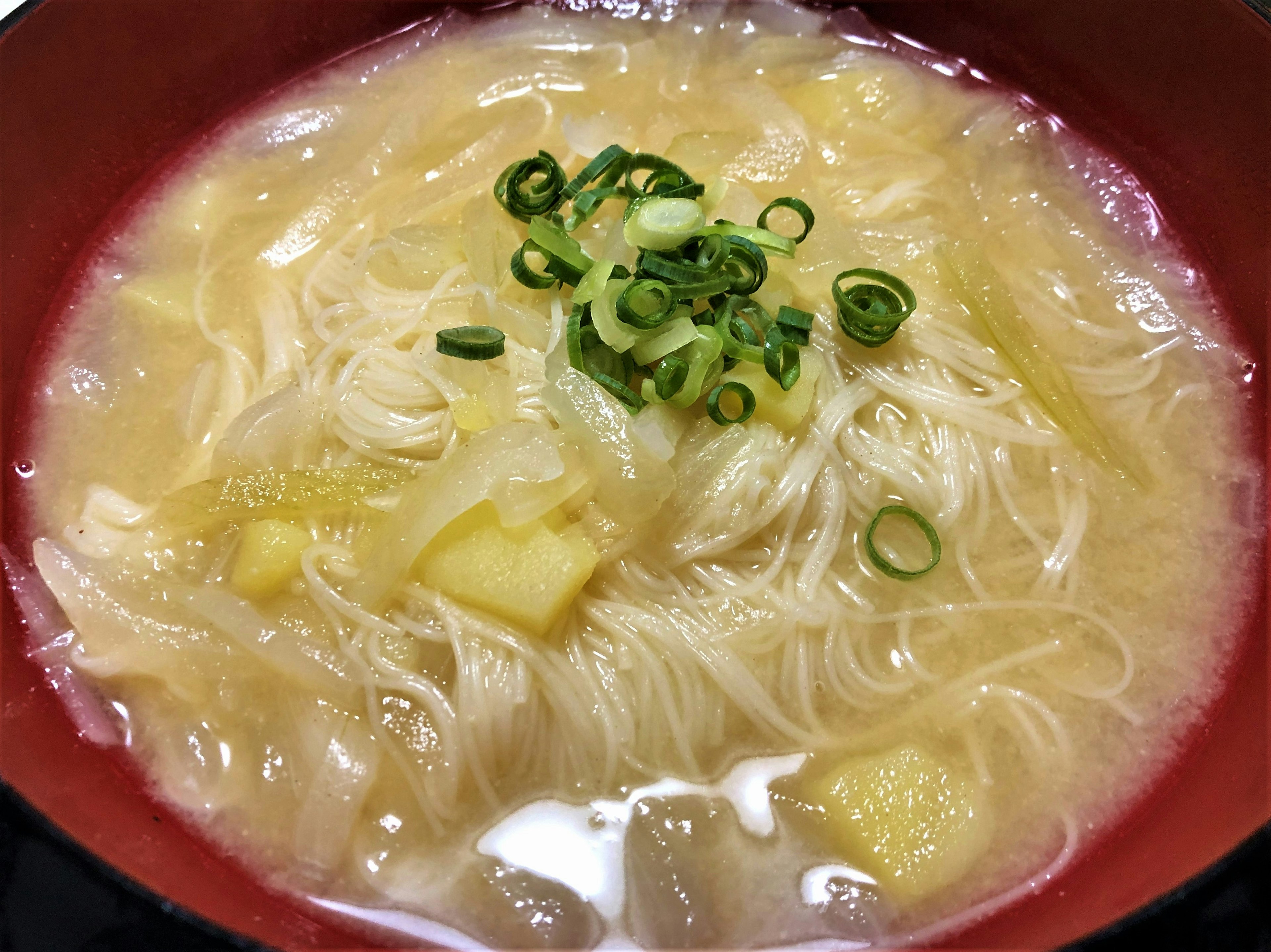 A bowl of clear soup with thin noodles and chopped green onions on top