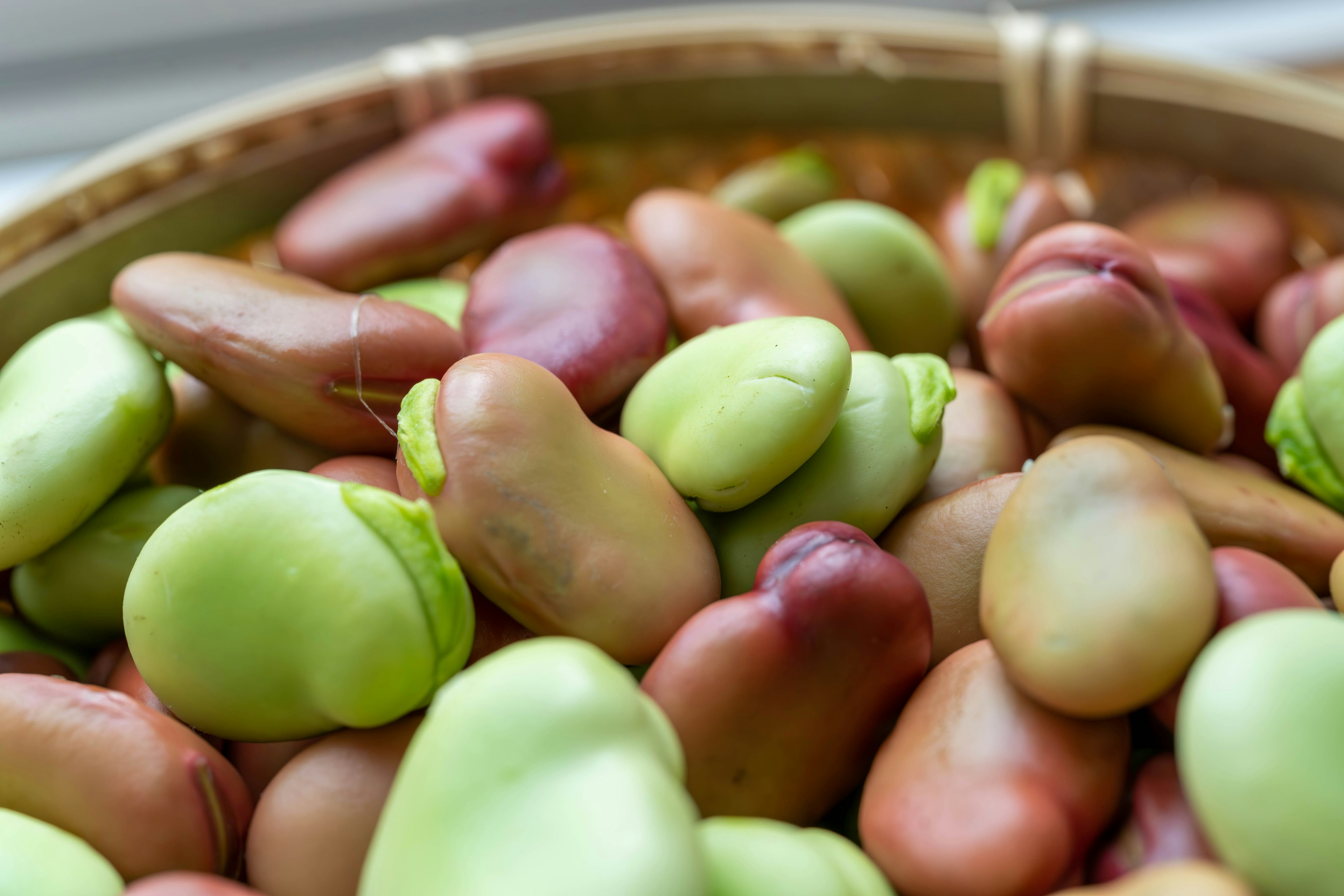 A close-up of green and reddish-brown beans in a bamboo basket