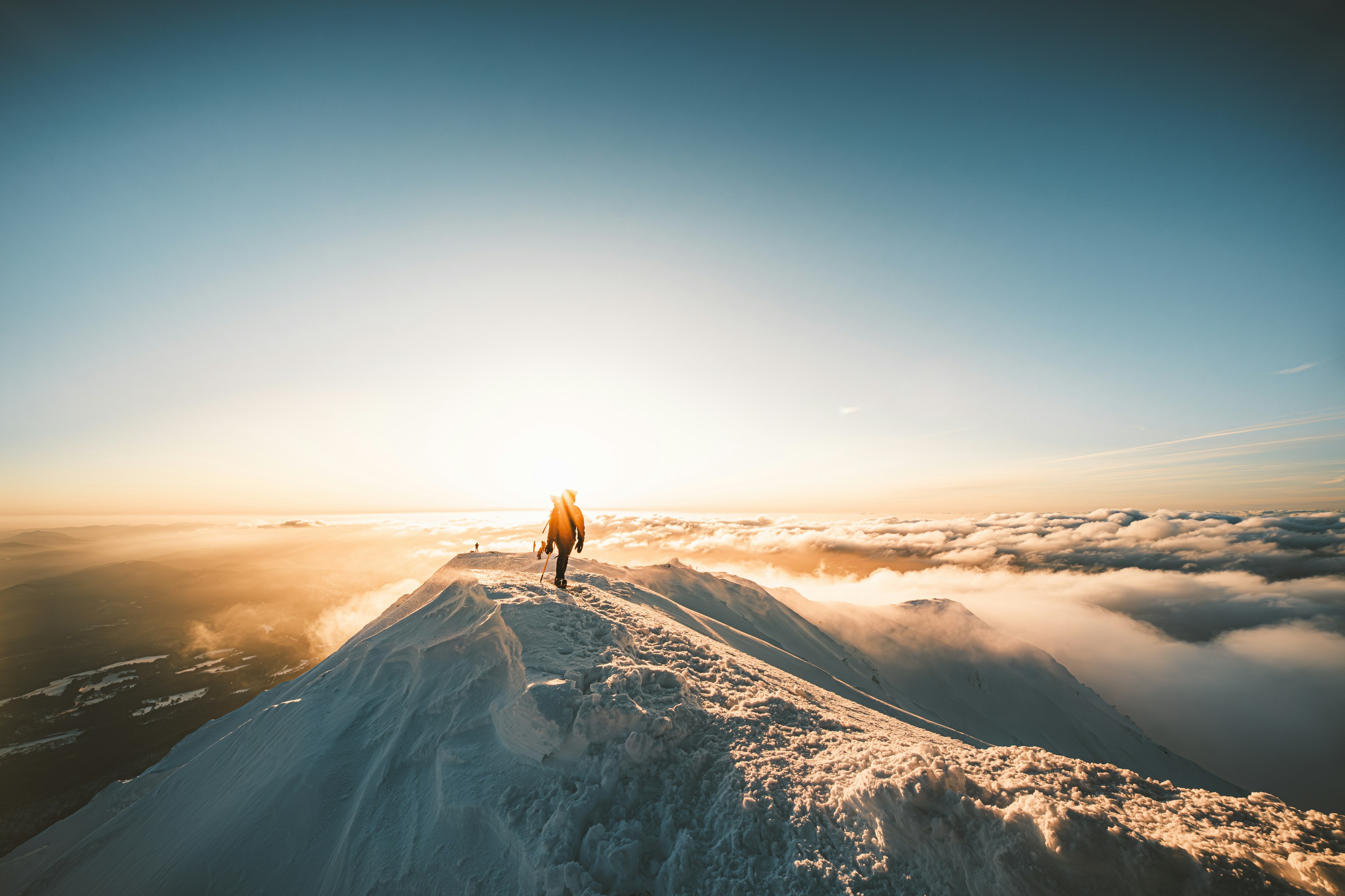 Person steht auf einem schneebedeckten Berggipfel bei Sonnenuntergang