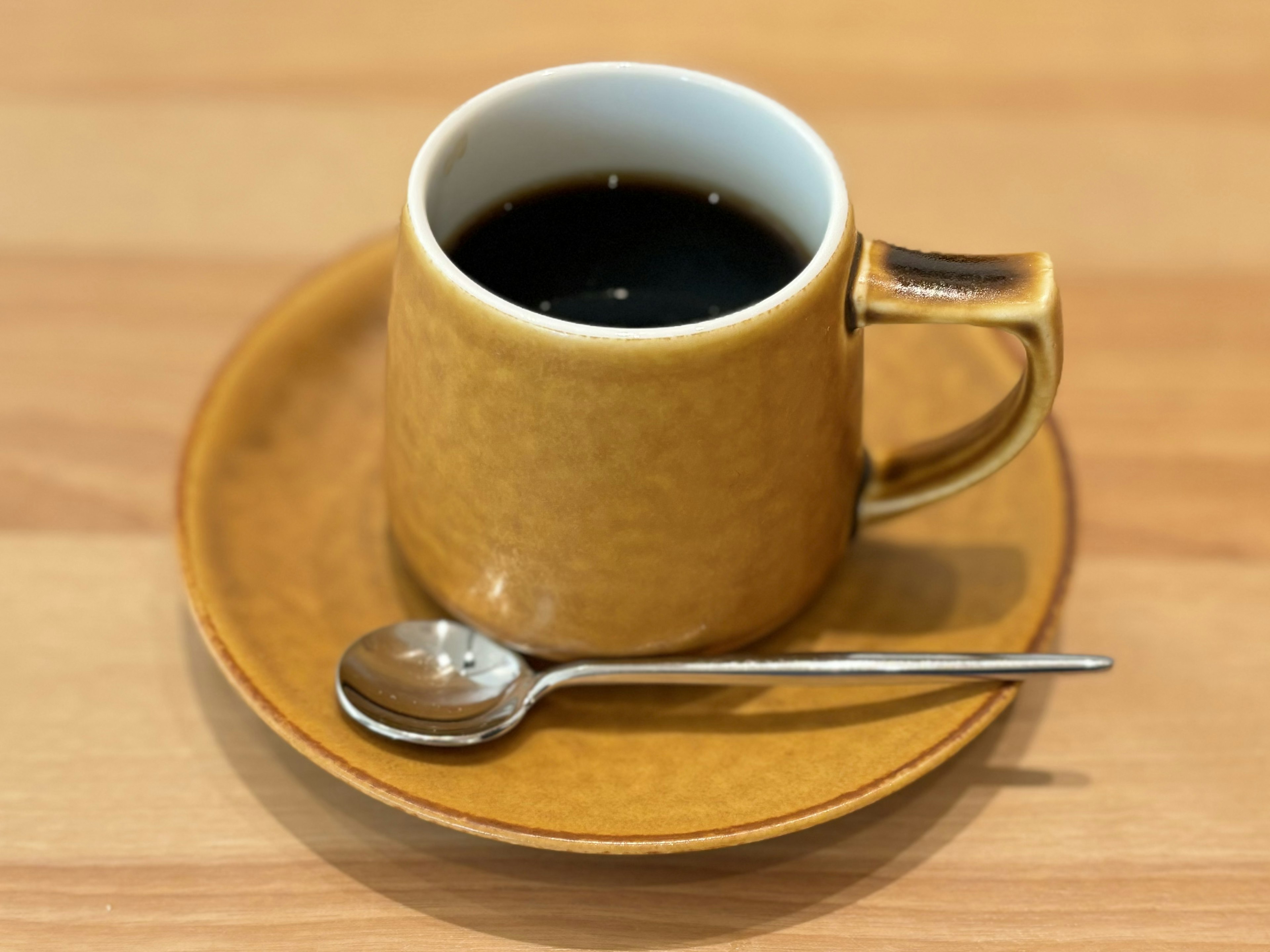 Taza amarilla de café en un platillo con una cuchara de plata