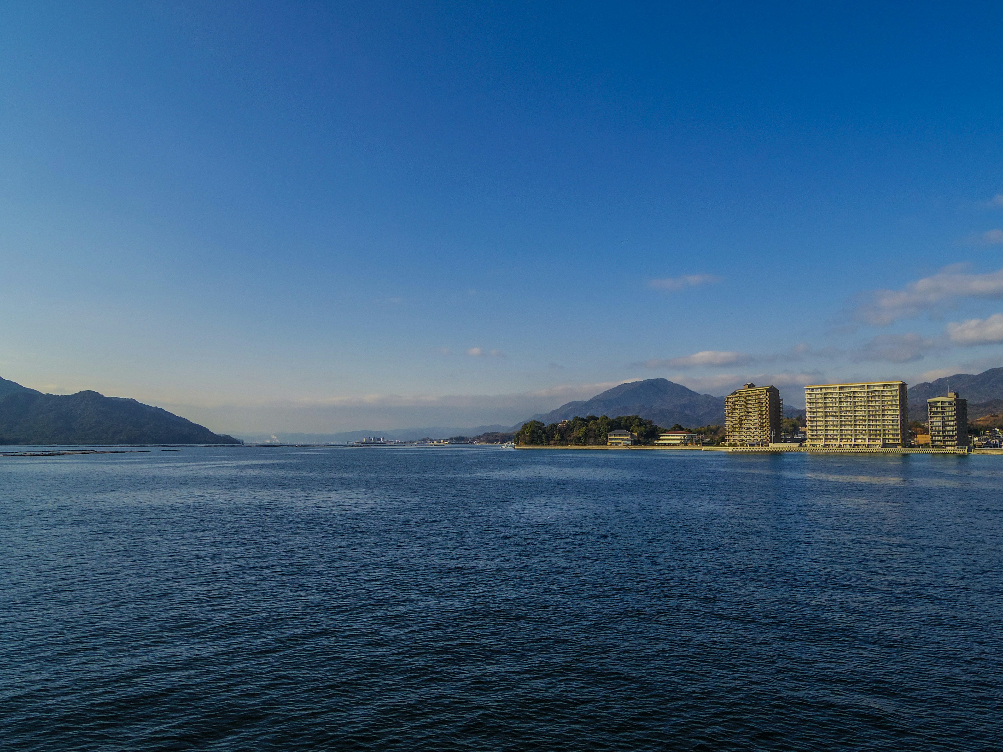 Vue panoramique avec un ciel bleu et une eau calme, montagnes et bâtiments au loin