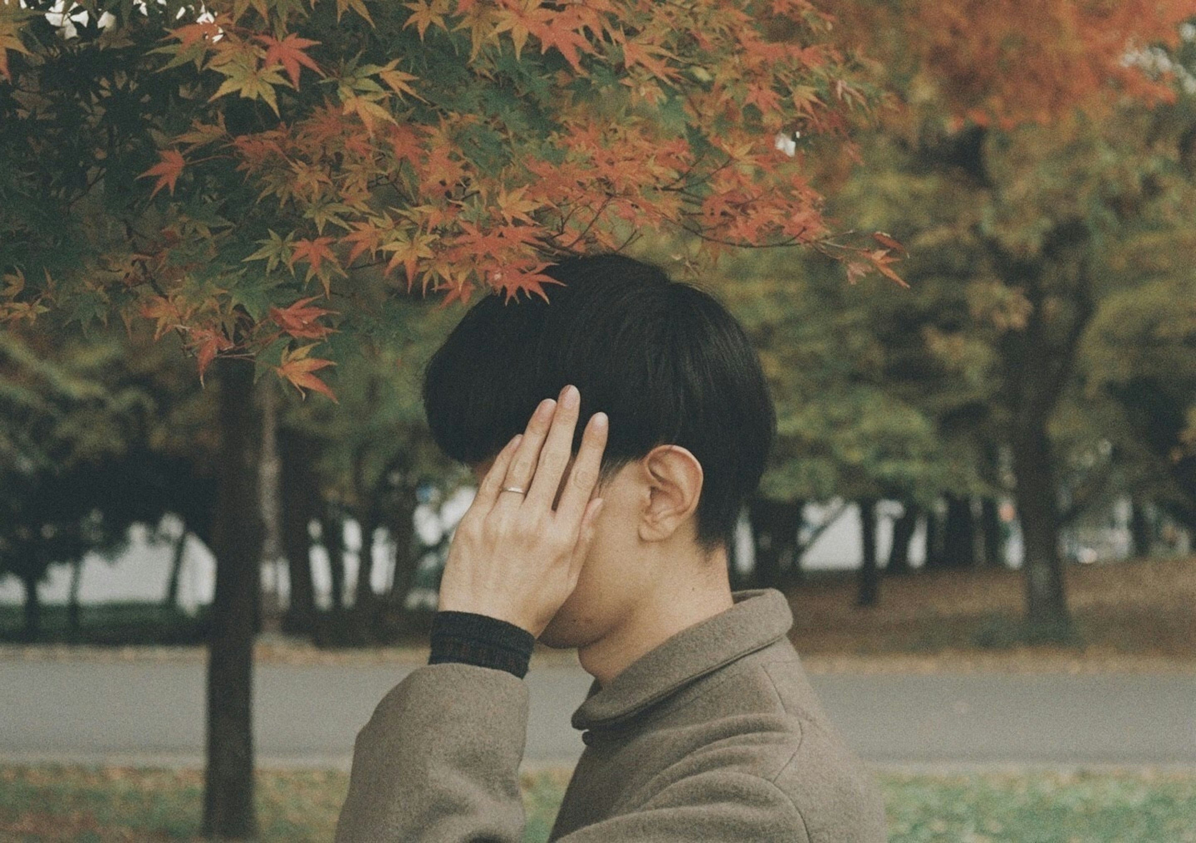 A man covering his face with his hand among autumn leaves