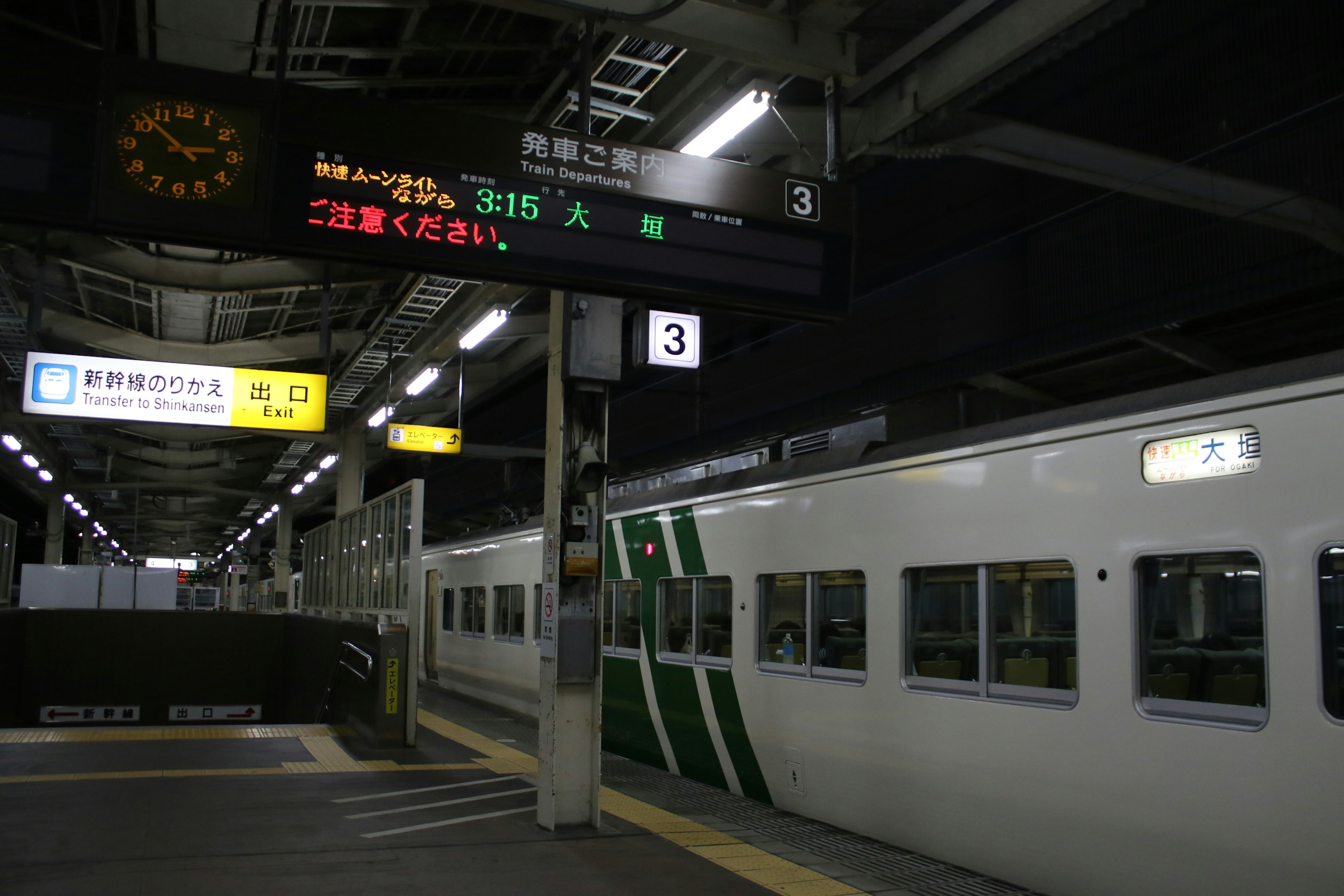 夜の駅で停車中の緑のラインの電車と表示板