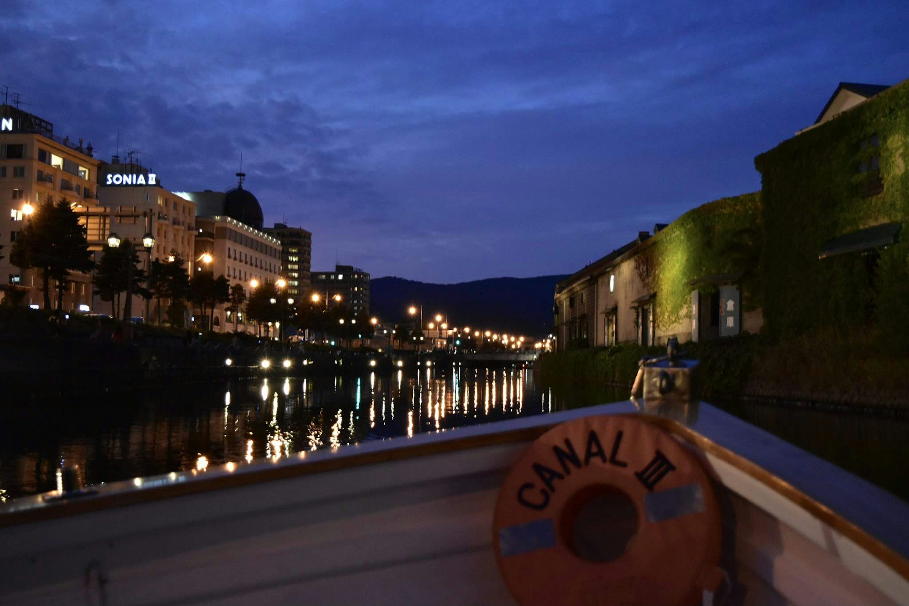 Premier plan d'un bateau sur un canal reflétant les lumières de la ville la nuit