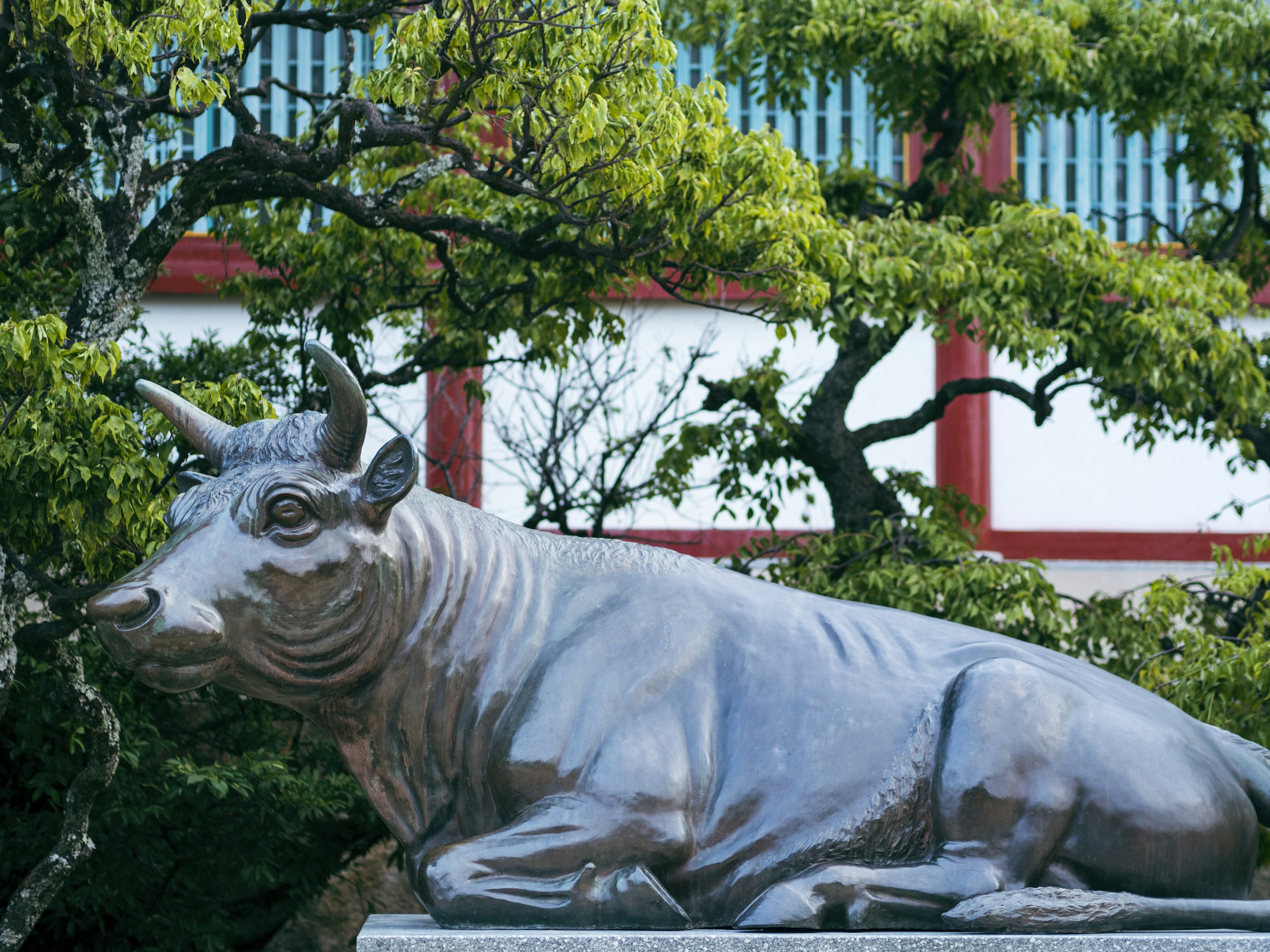 Une sculpture de taureau en bronze dans un jardin verdoyant avec une architecture traditionnelle