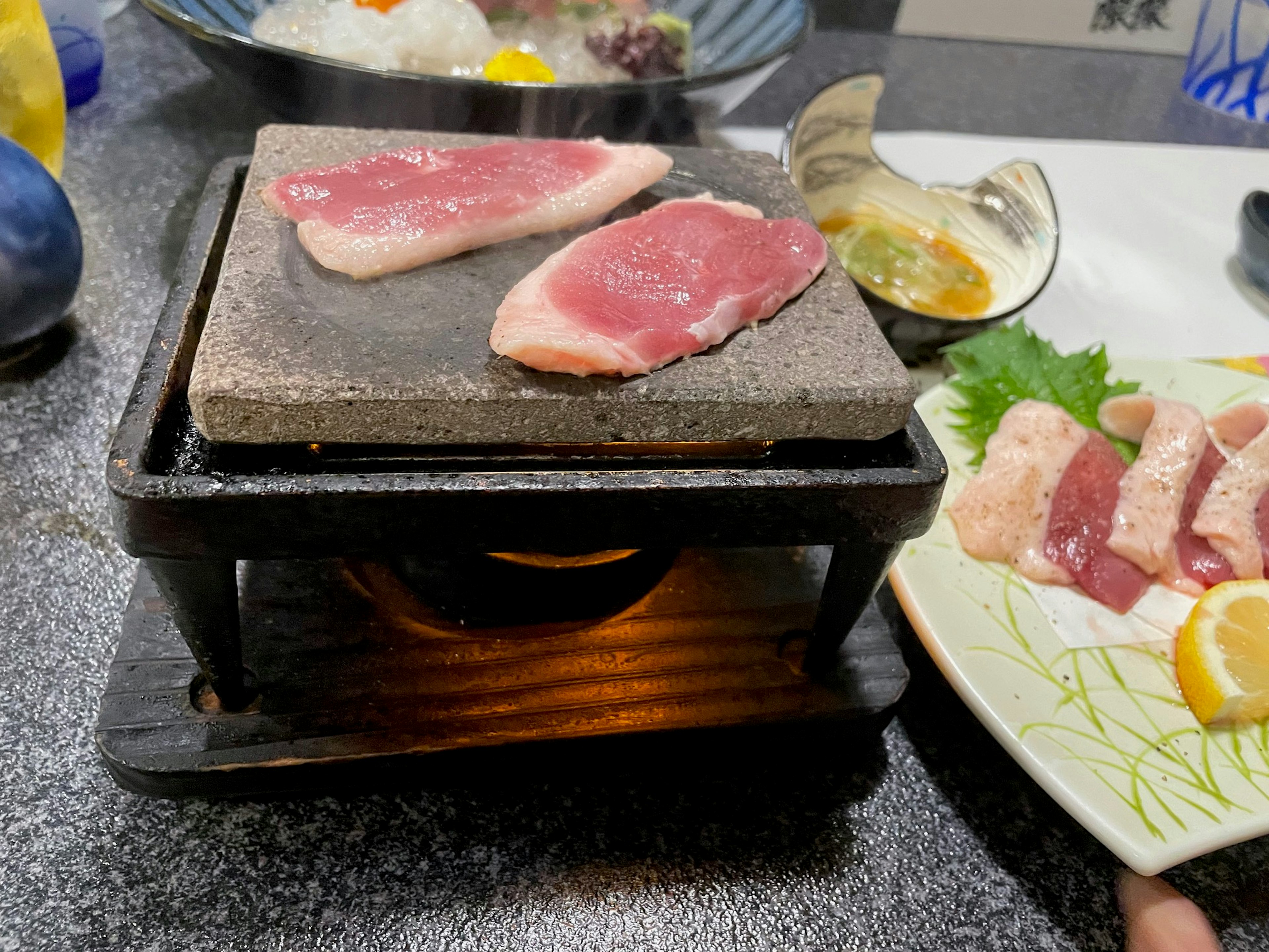 焼き石の上にある薄切りの肉と周囲の料理