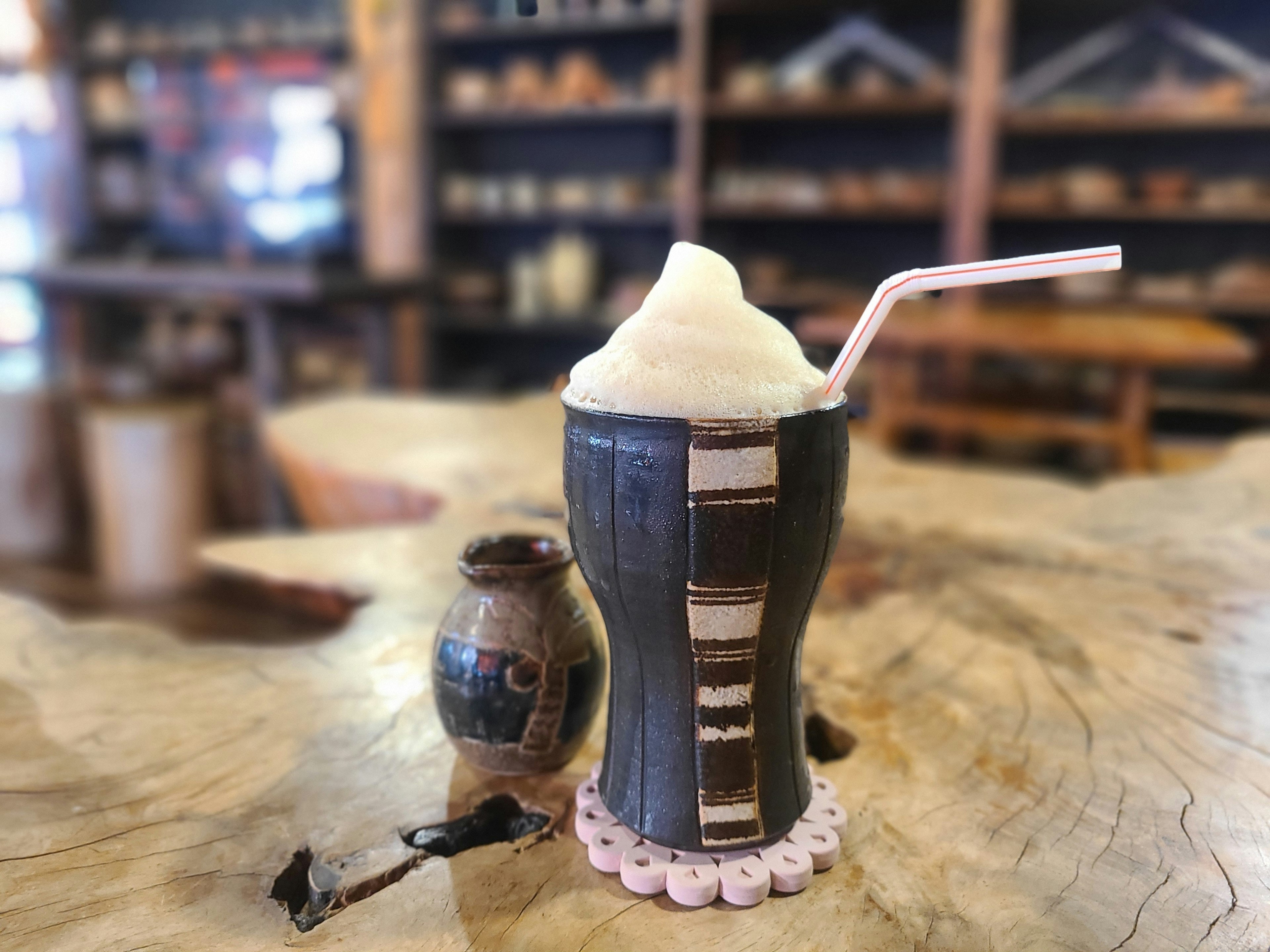 Frothy drink in a decorative cup on a wooden table with a small pottery jar