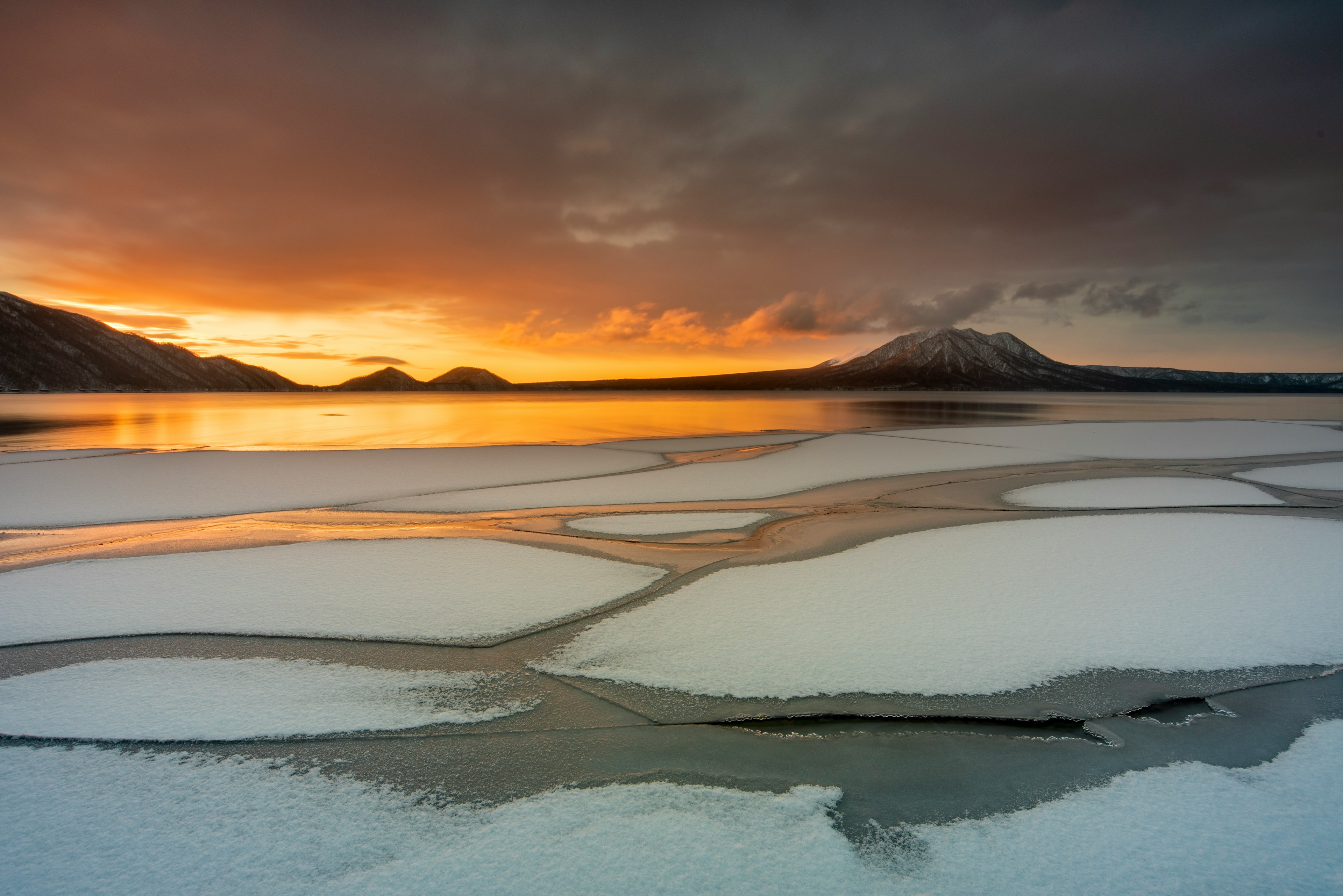 Gefrorene Seenlandschaft mit orangefarbenem Sonnenuntergang und Bergsilhouette