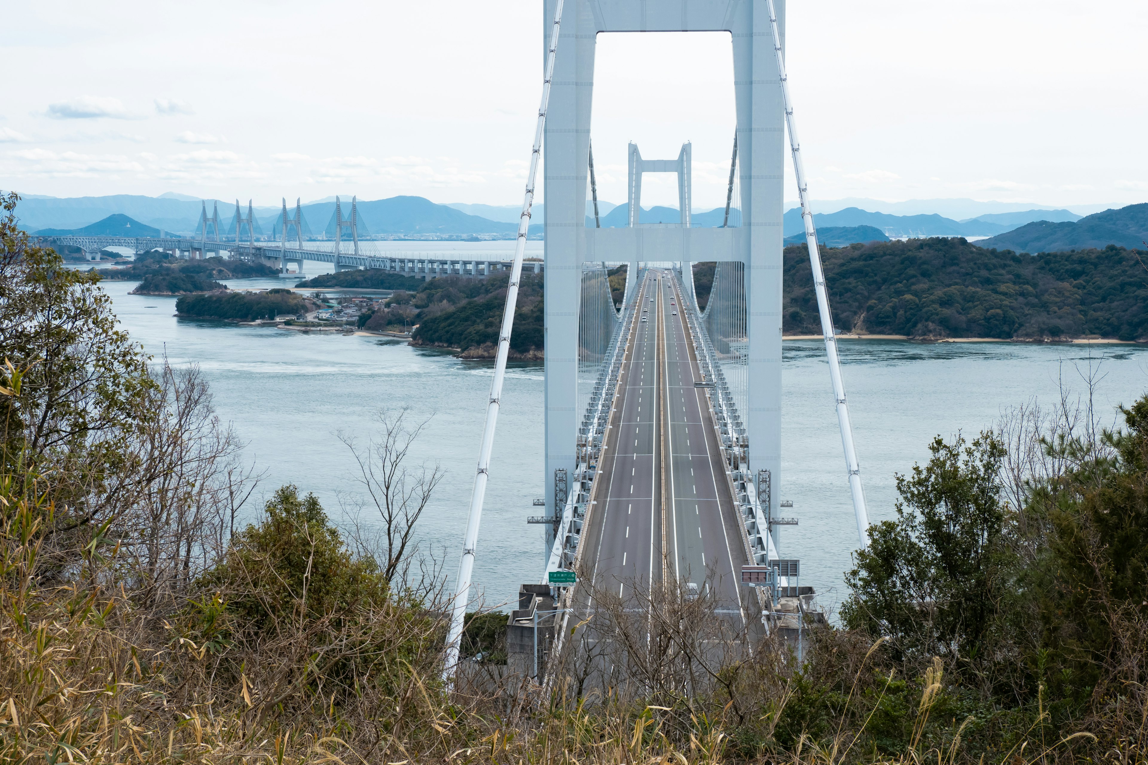 Un puente blanco que se extiende sobre un paisaje hermoso con montañas y aguas tranquilas al fondo