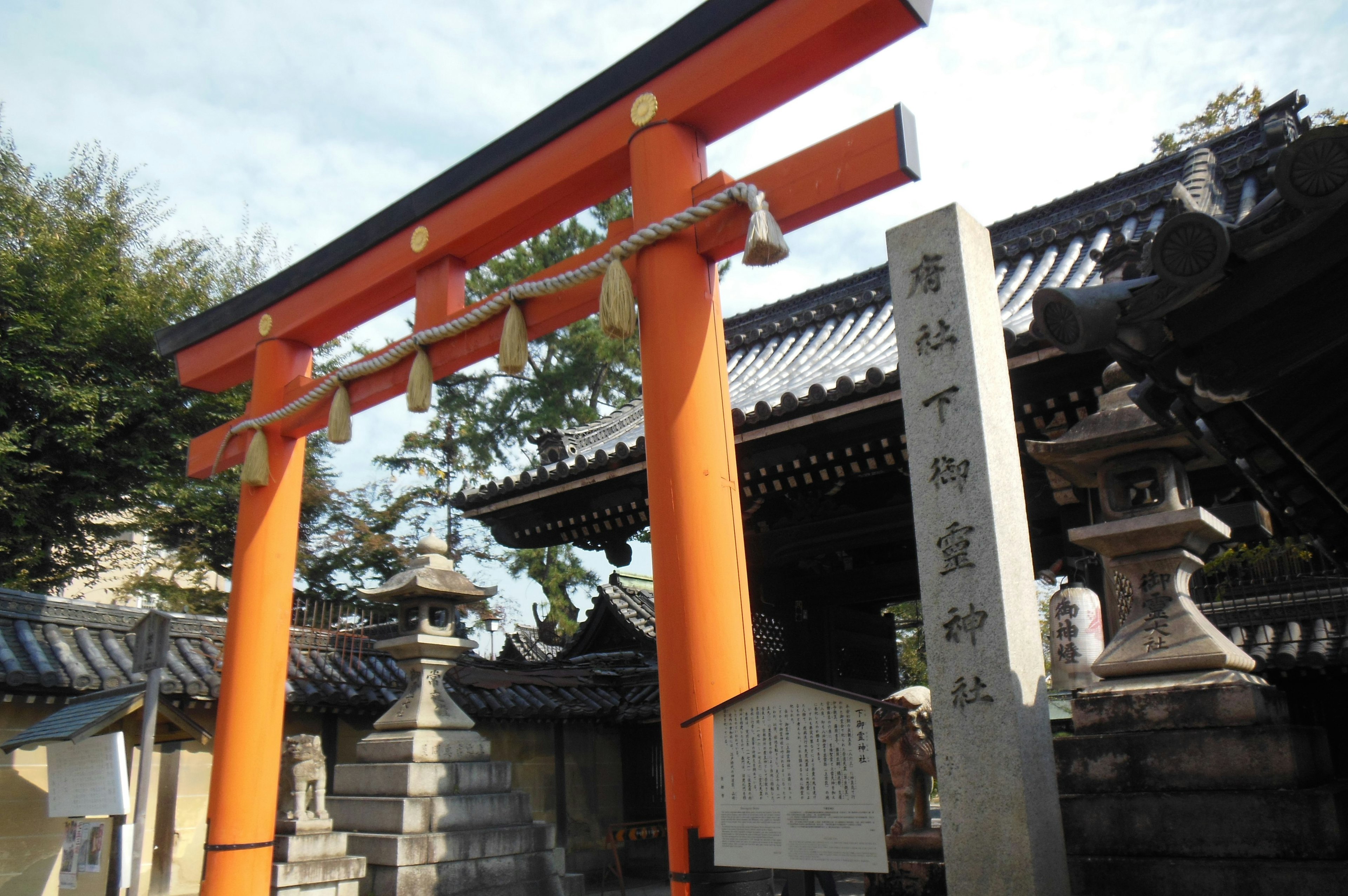 Entrance of a Japanese shrine featuring an orange torii gate and a stone monument