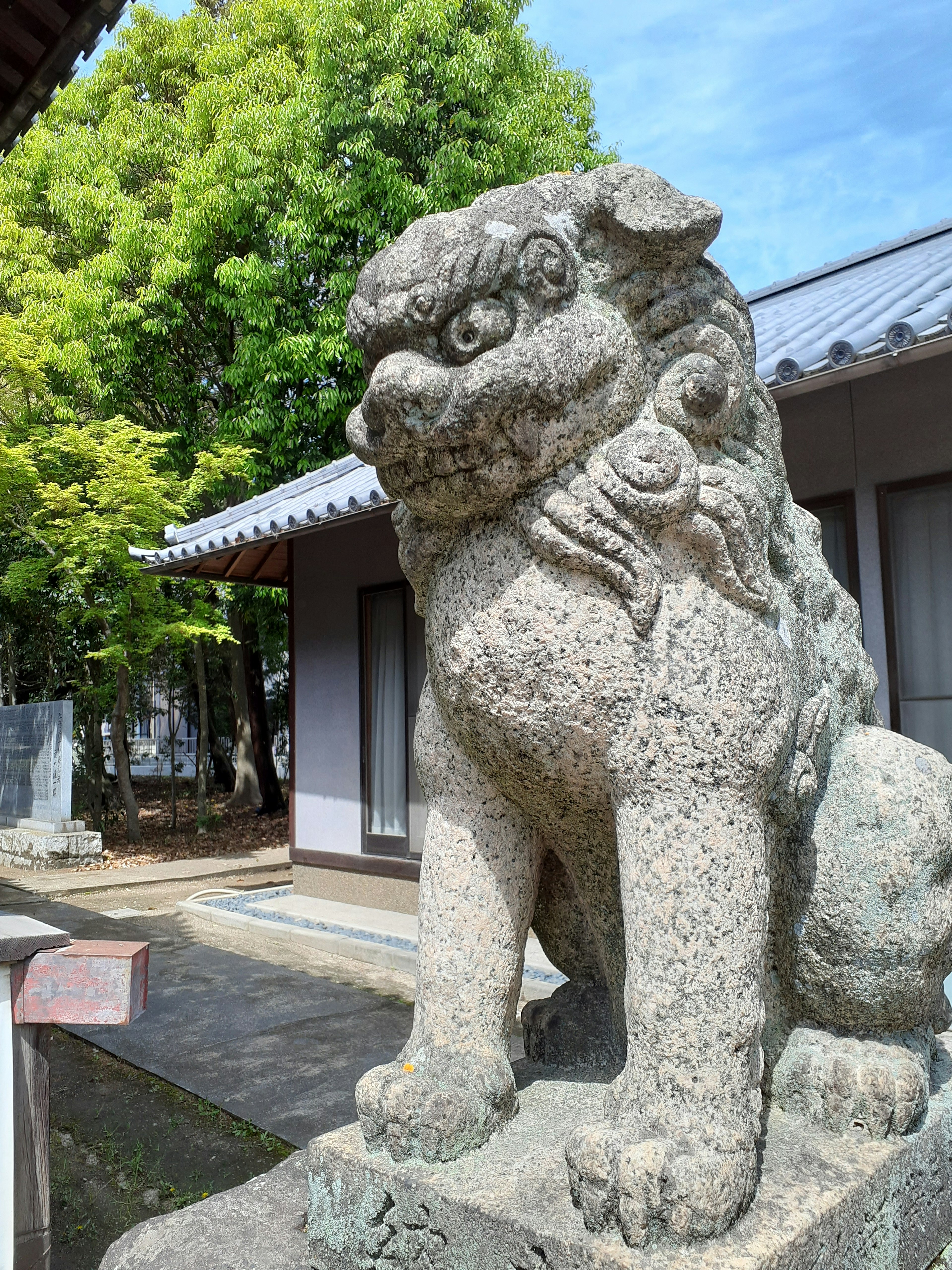 Stone komainu statue standing in front of a shrine with green trees in the background