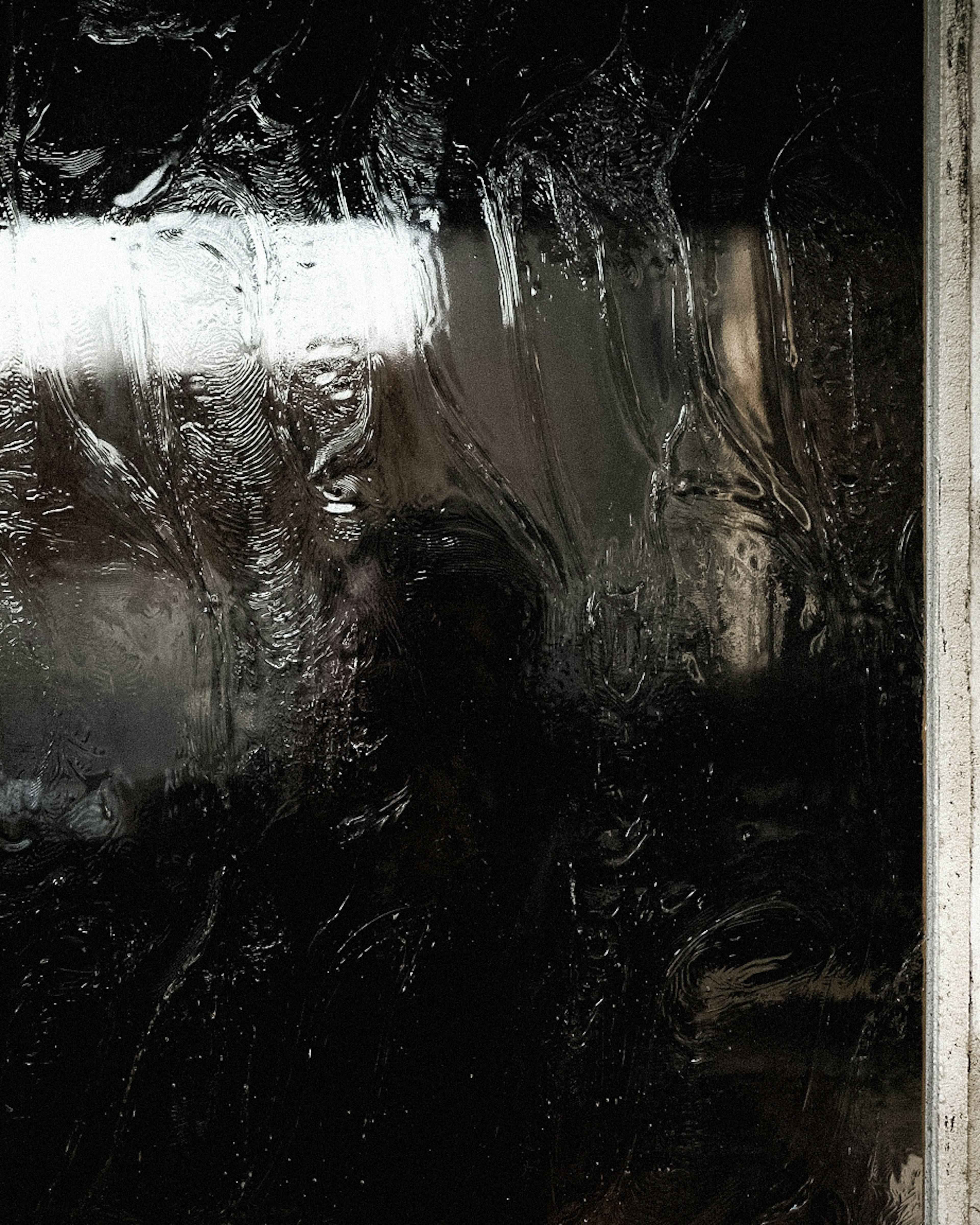 A wet window surface with water droplets and a blurred figure behind it