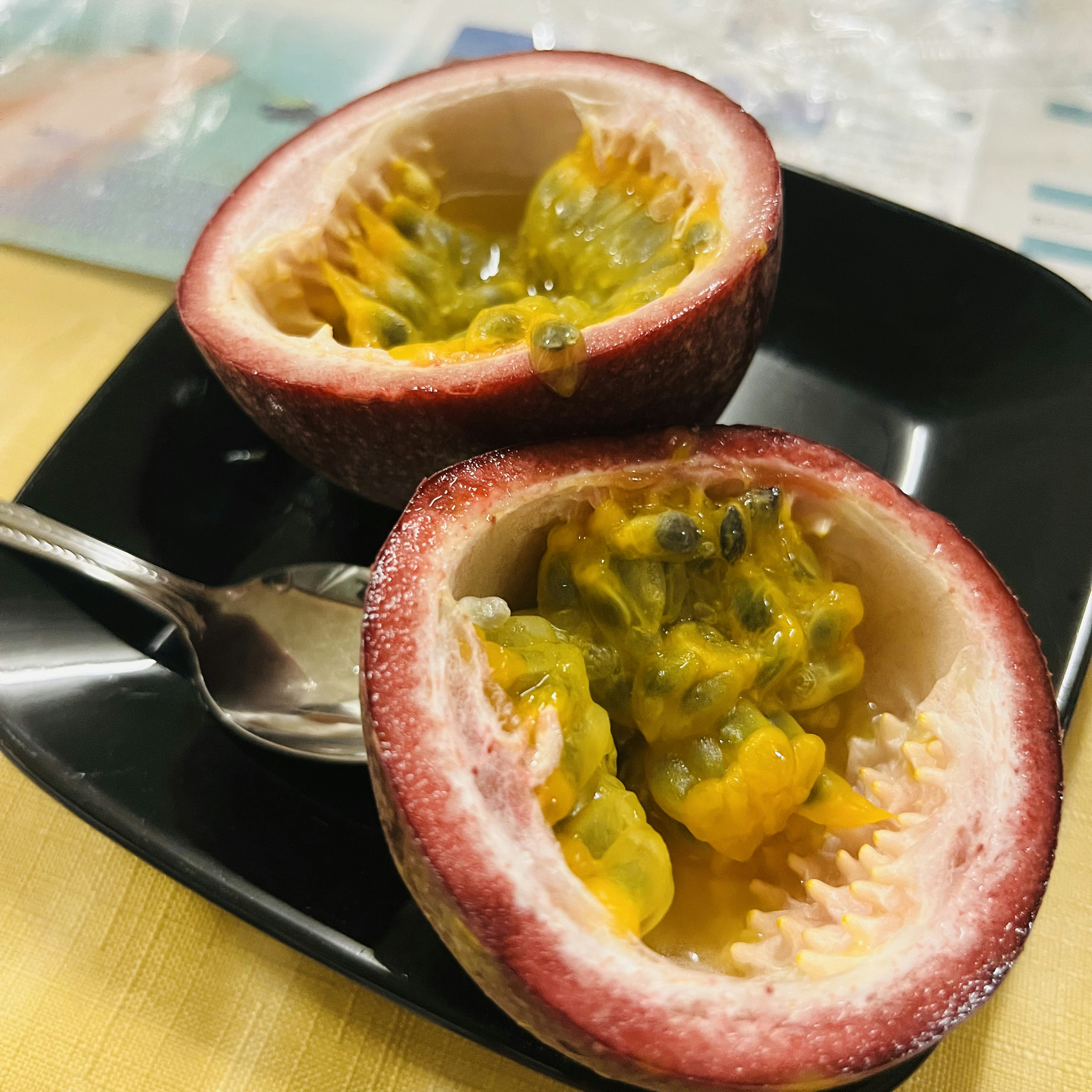 Cut passion fruit displayed on a black plate with a spoon