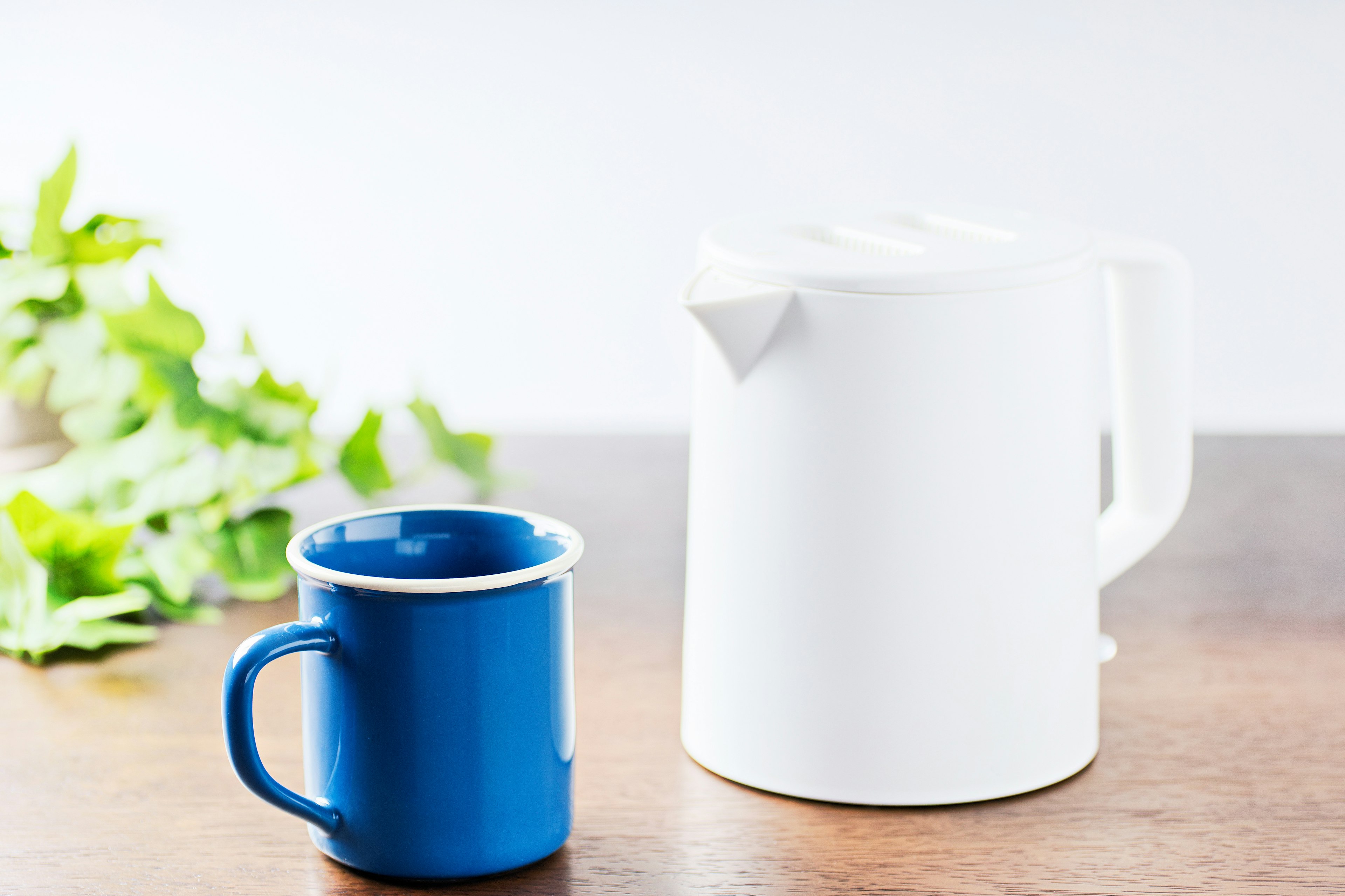 A white teapot and a blue mug placed on a wooden table