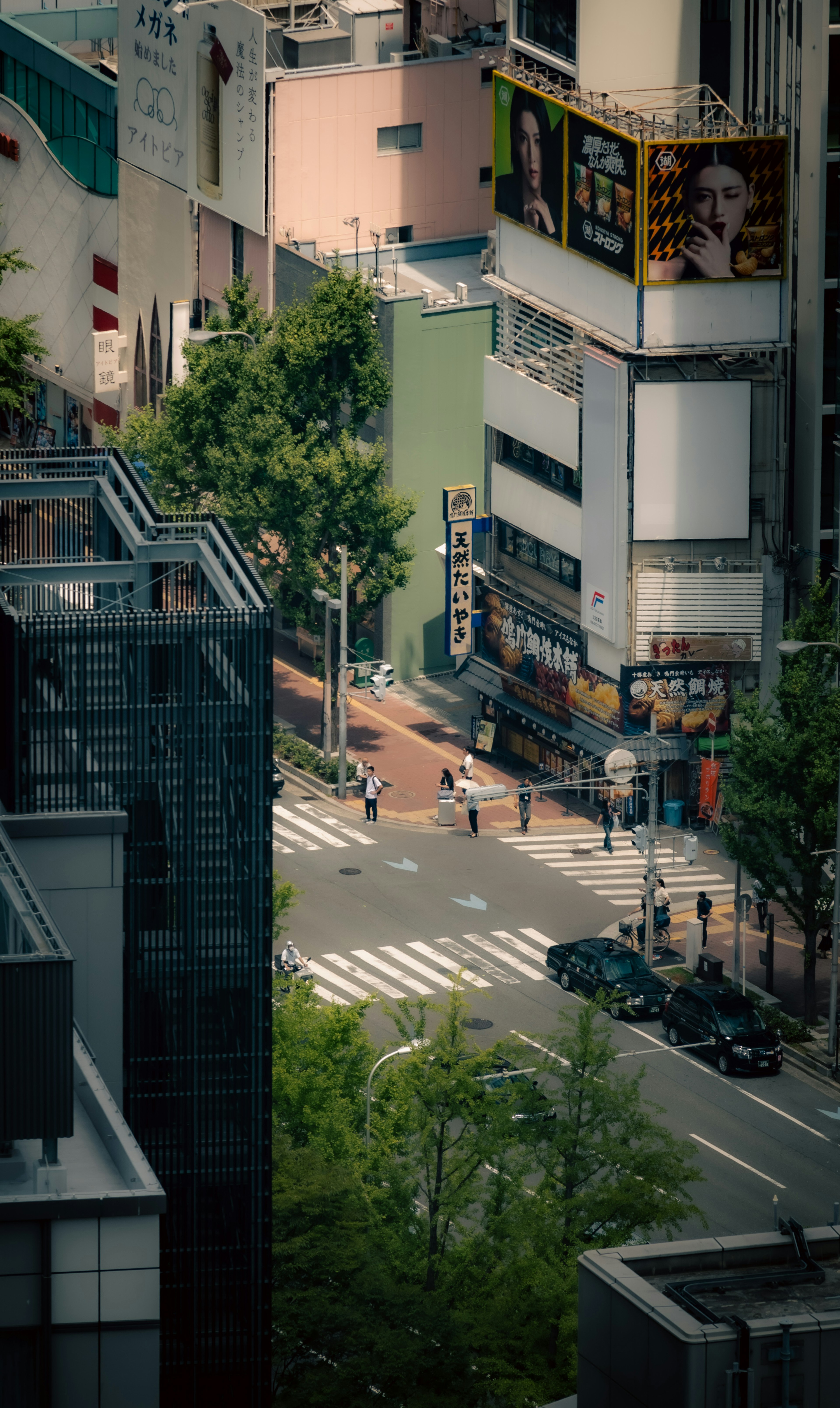 Aerial view of an urban intersection with green trees and pedestrians