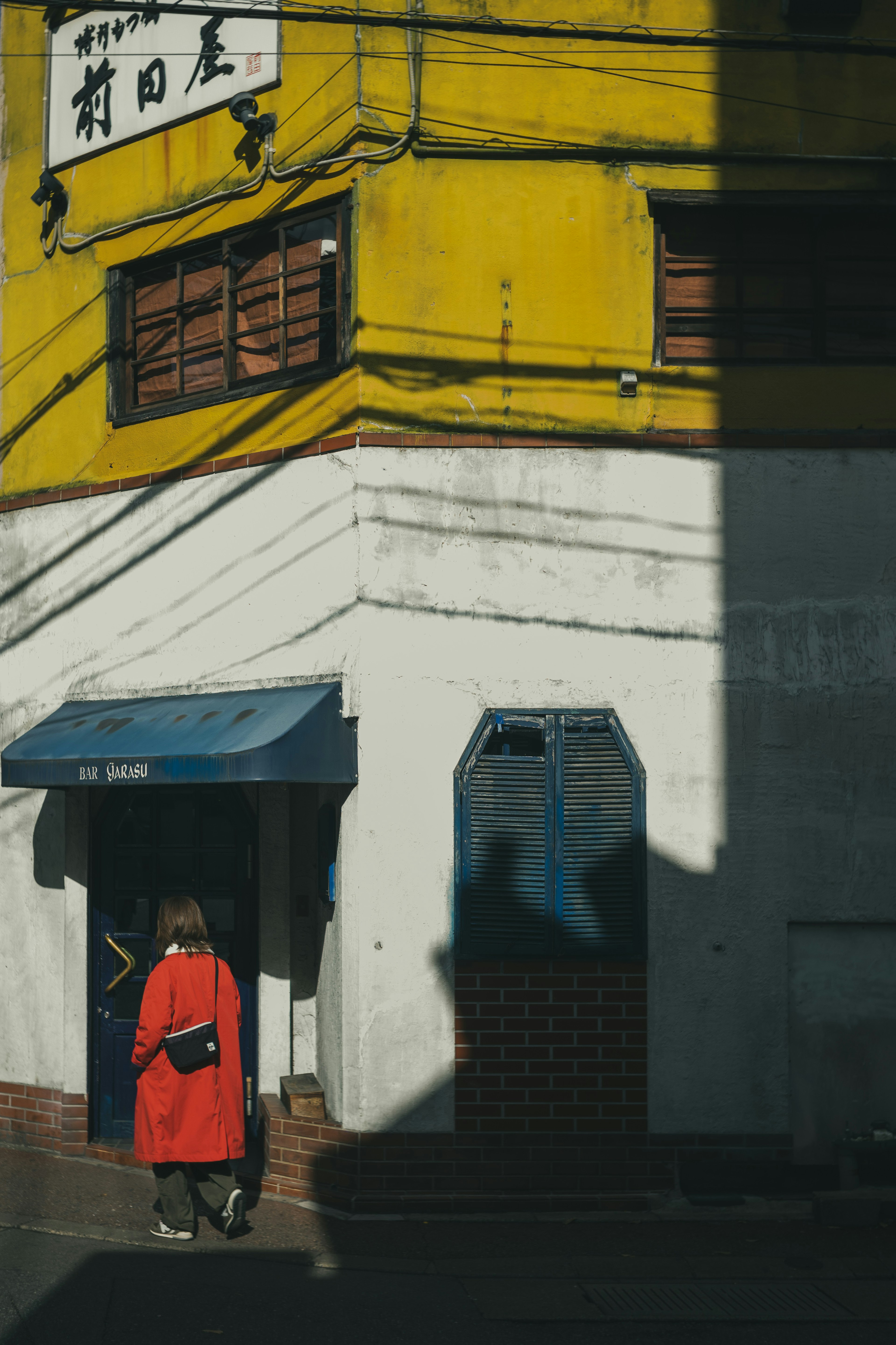 Seorang wanita berpakaian merah berdiri di sudut bangunan dengan dinding kuning