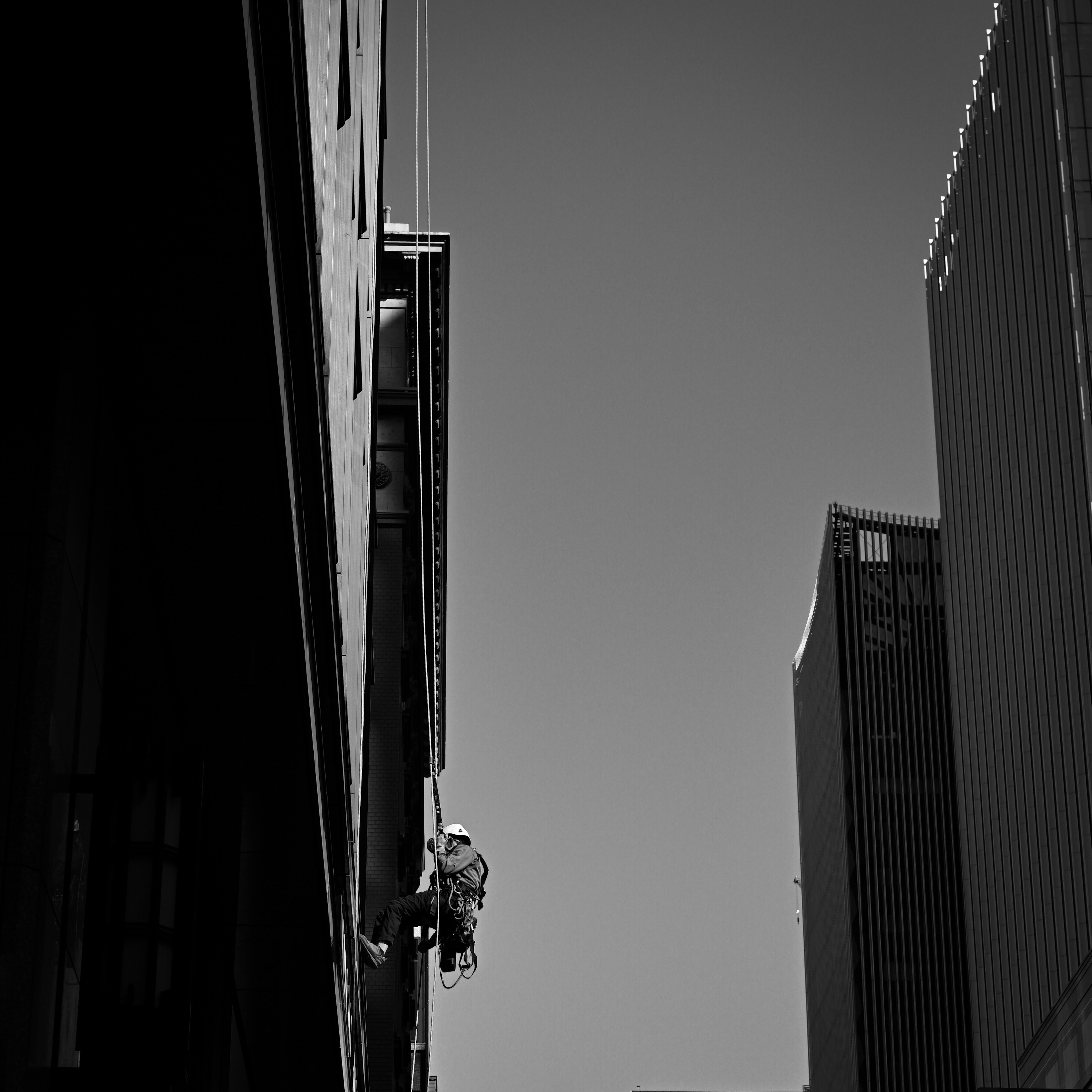 Black and white image of a worker climbing a building wall