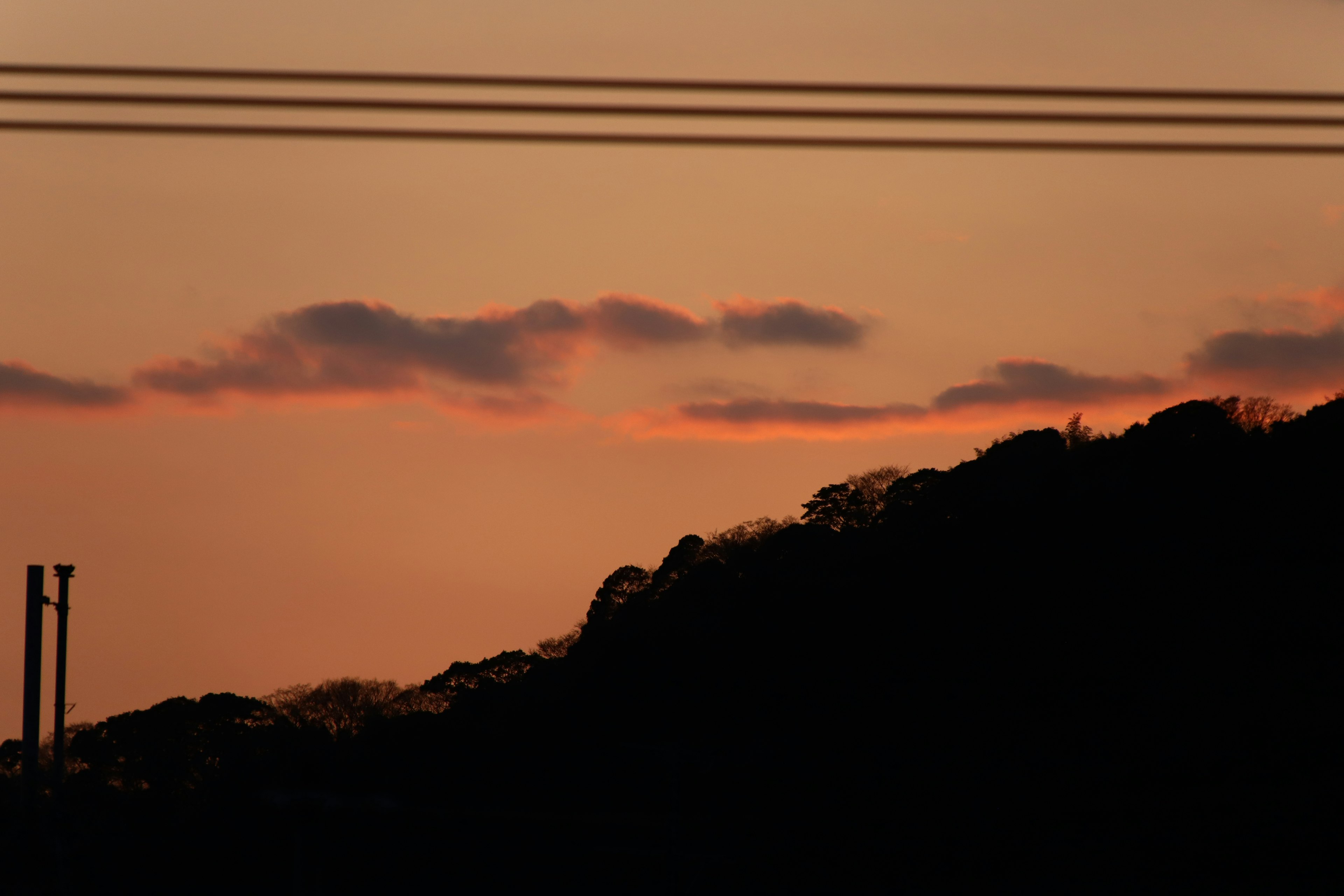 Ein Sonnenuntergangshimmel mit silhouettierten Hügeln und Stromleitungen