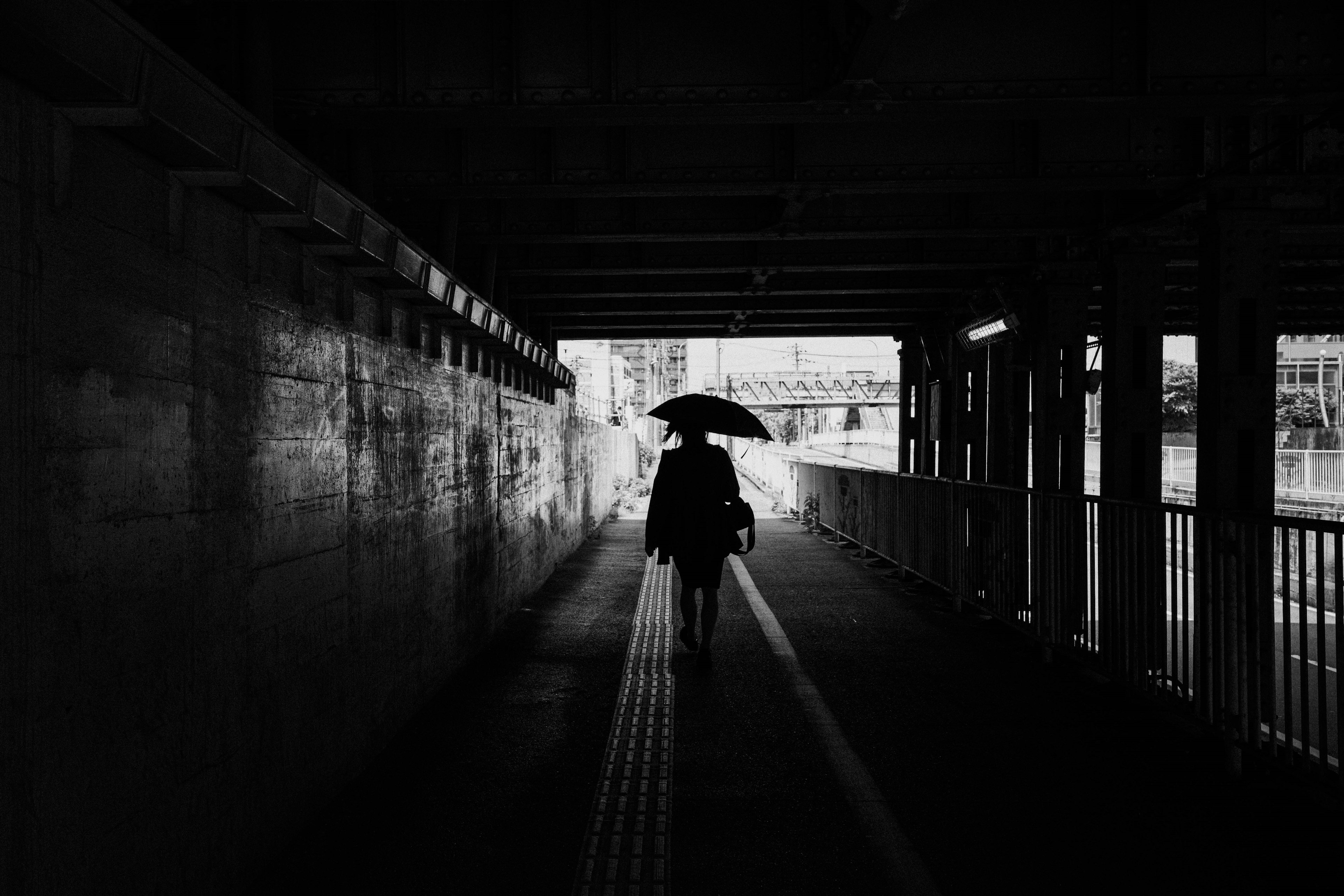 Silhouette di una persona che cammina in un tunnel con un ombrello in bianco e nero