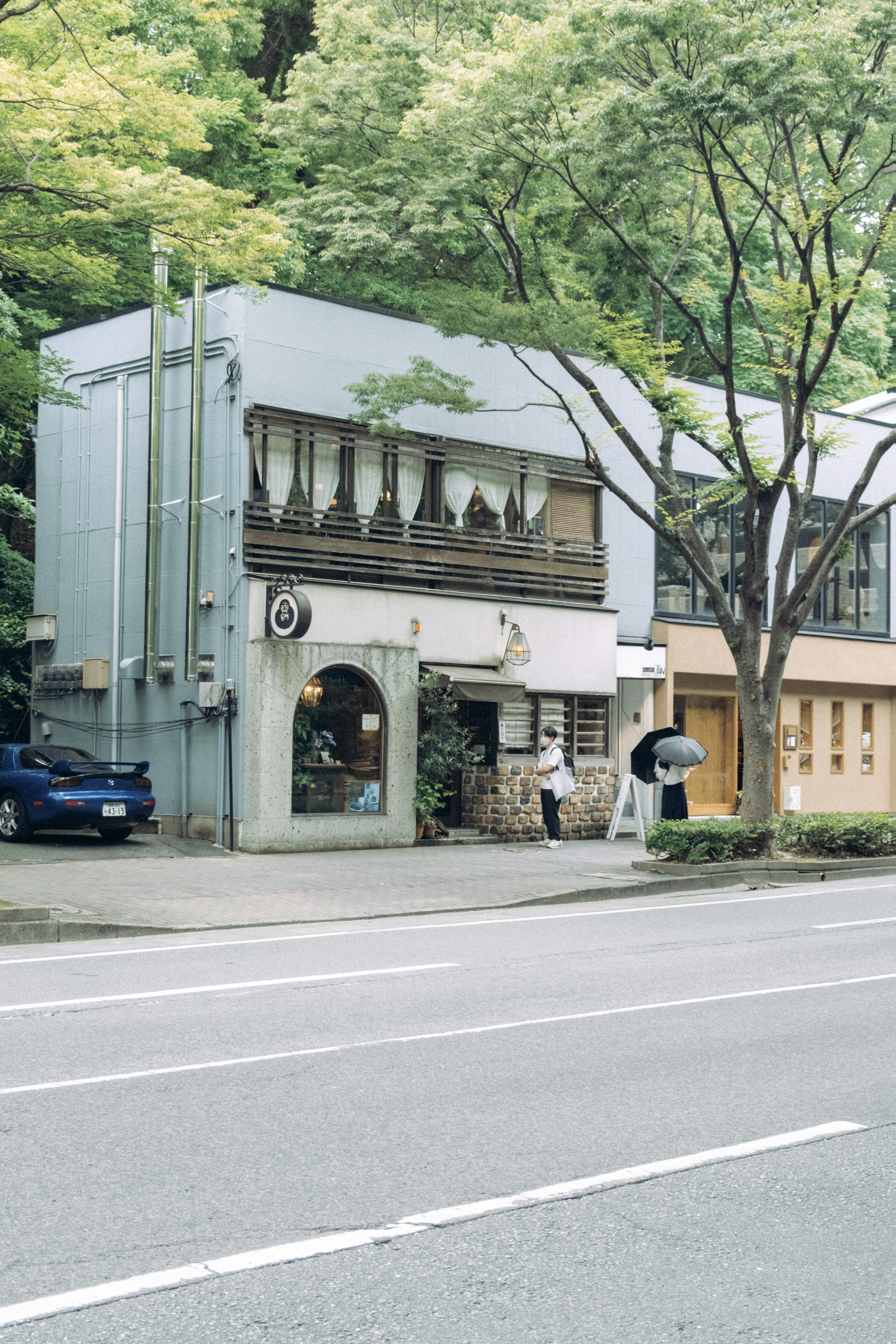 Fassade eines Cafés und eines modernen Gebäudes entlang einer von Bäumen gesäumten Straße