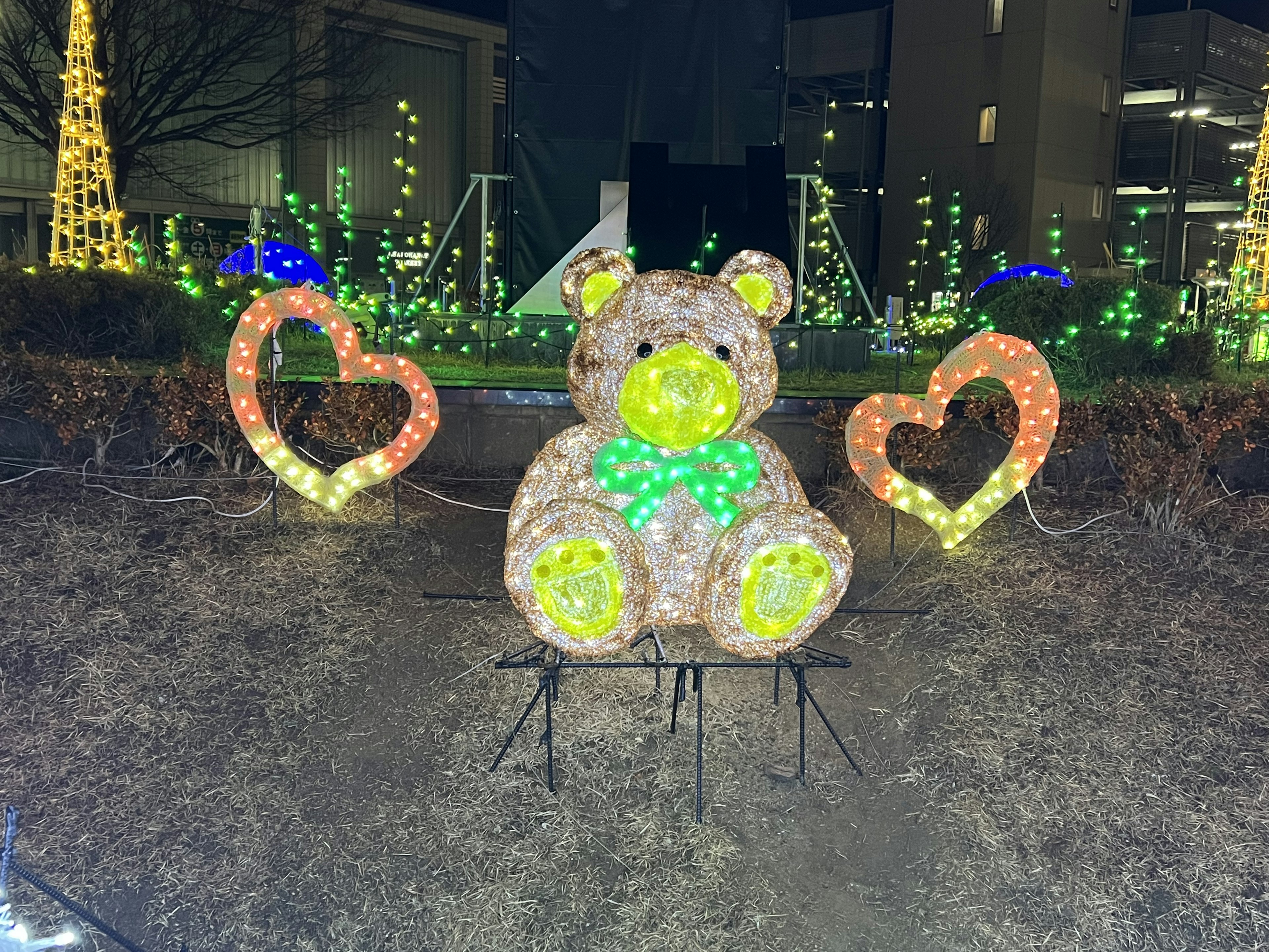 Sculpture d'ours en peluche illuminée avec des lumières en forme de cœur dans un parc nocturne