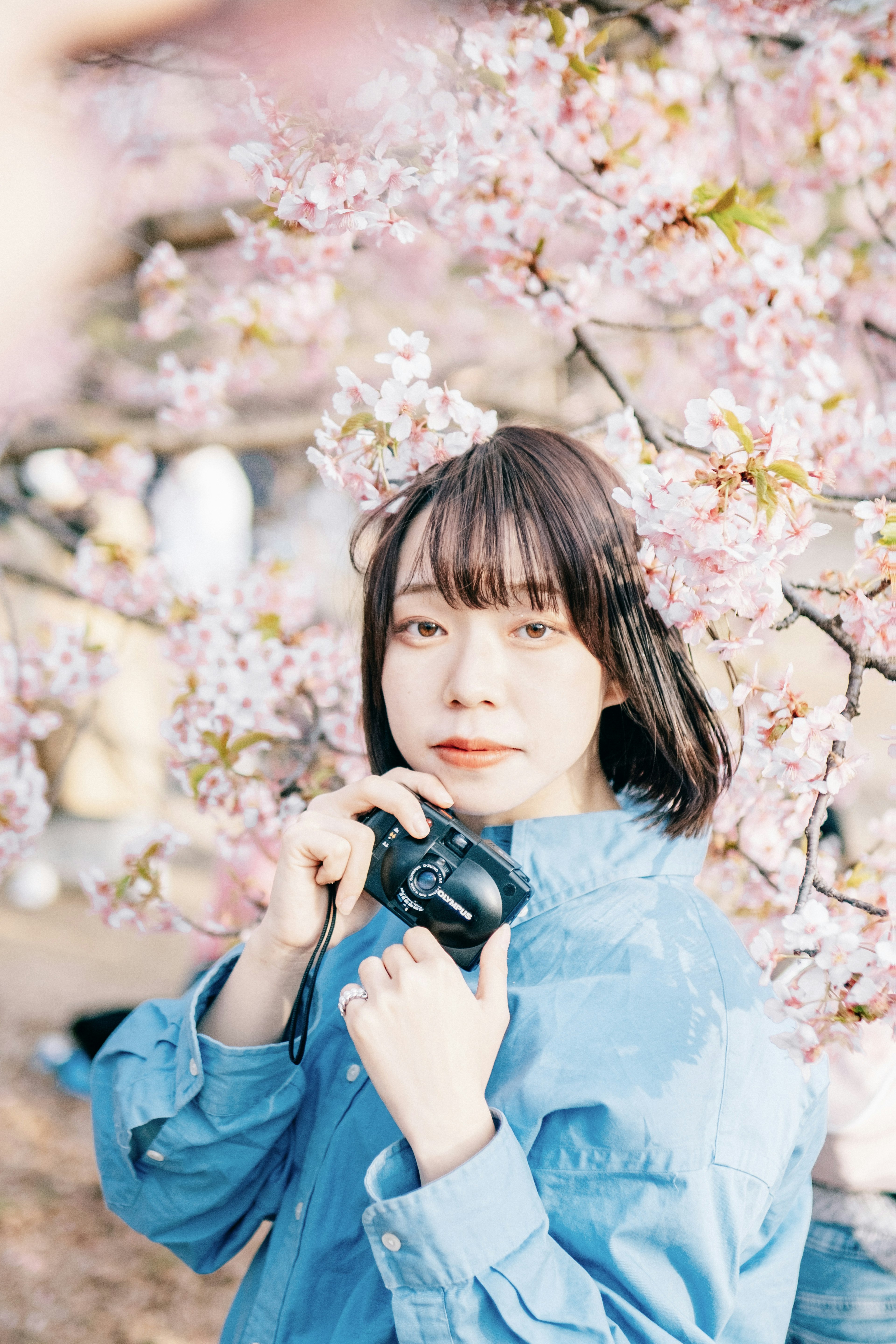 Retrato de una mujer sosteniendo una cámara frente a flores de cerezo