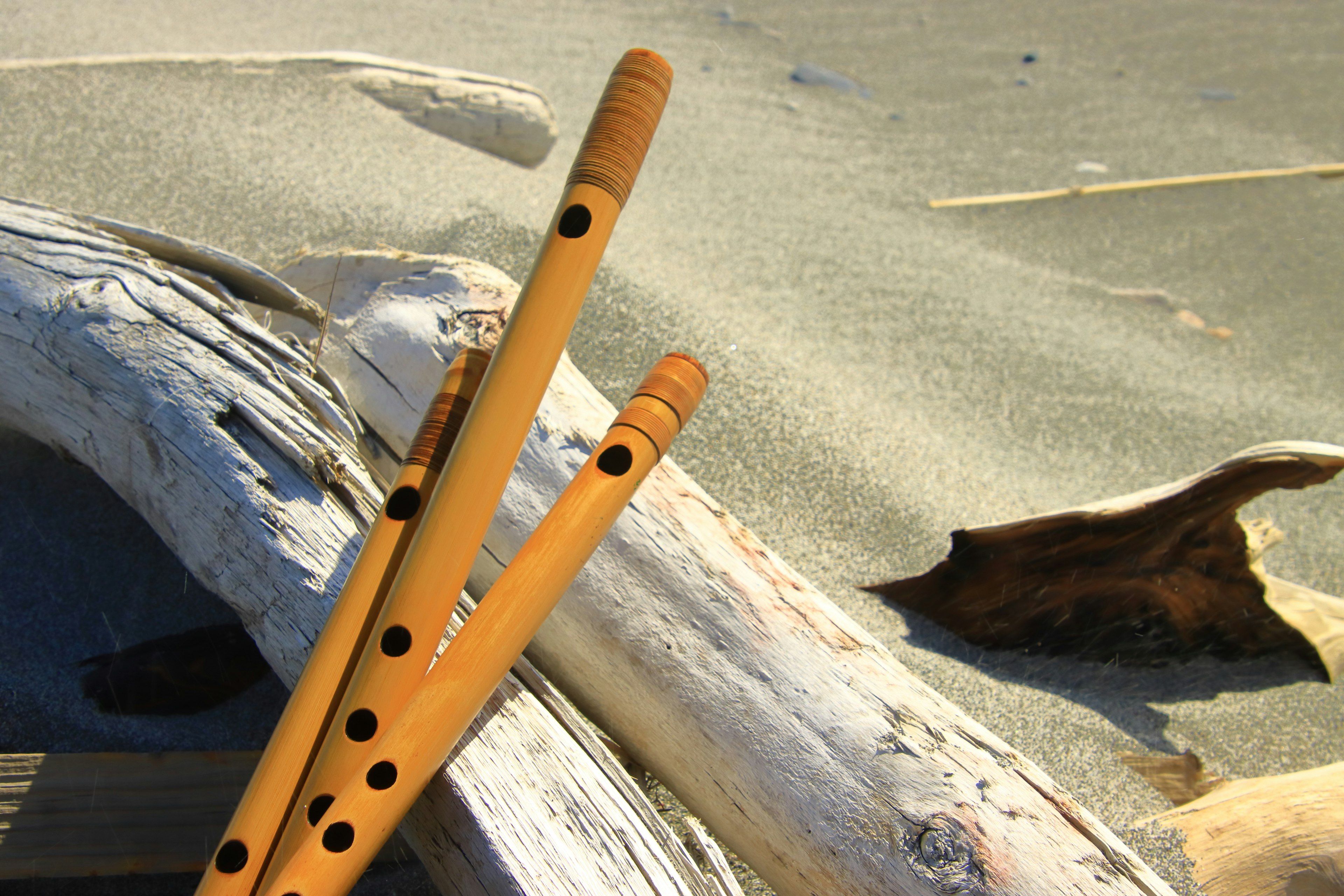 Two wooden flutes resting on a sandy beach with driftwood