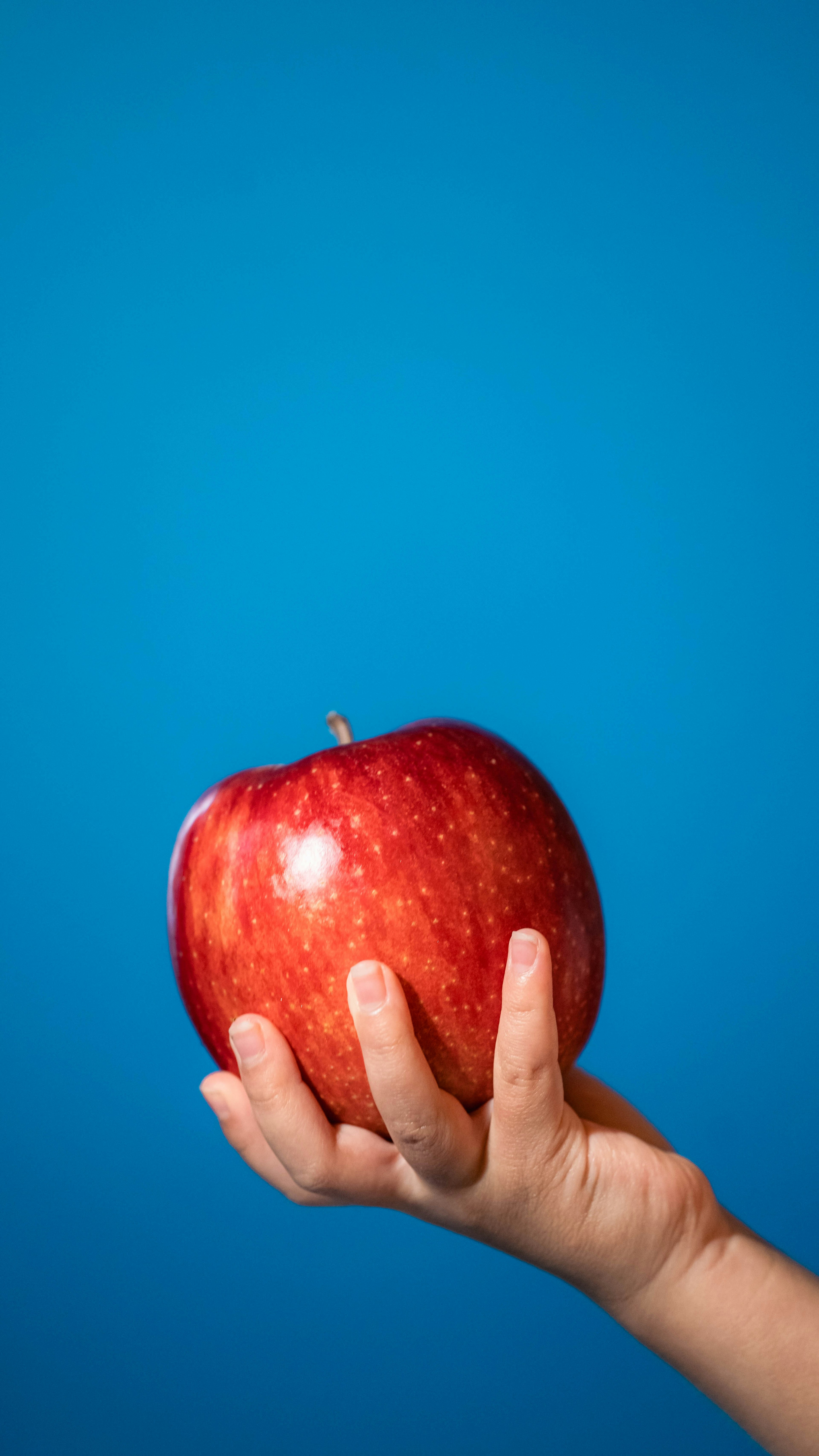 Una mano sosteniendo una manzana roja frente a un fondo azul