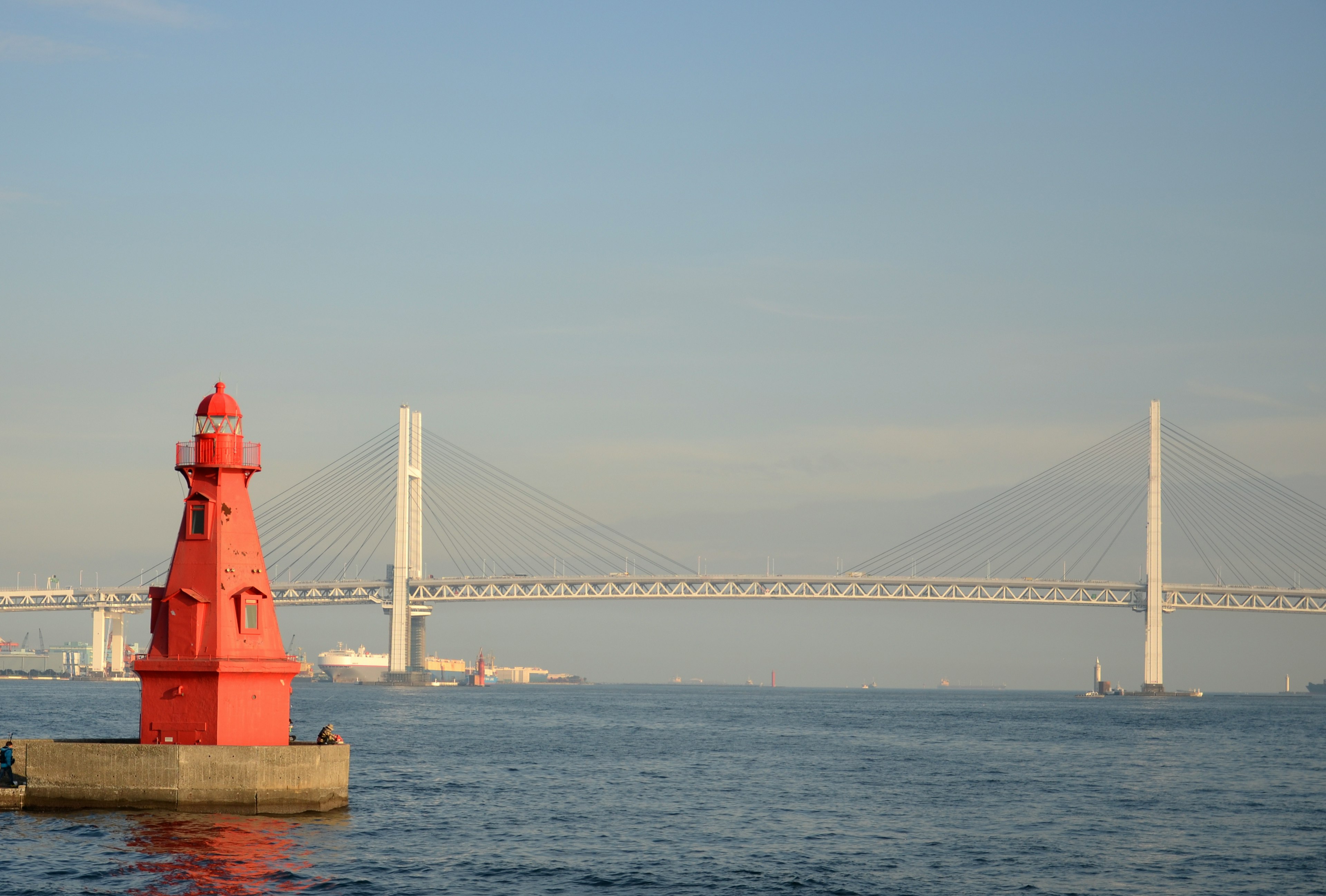 Red lighthouse near a bridge over calm waters