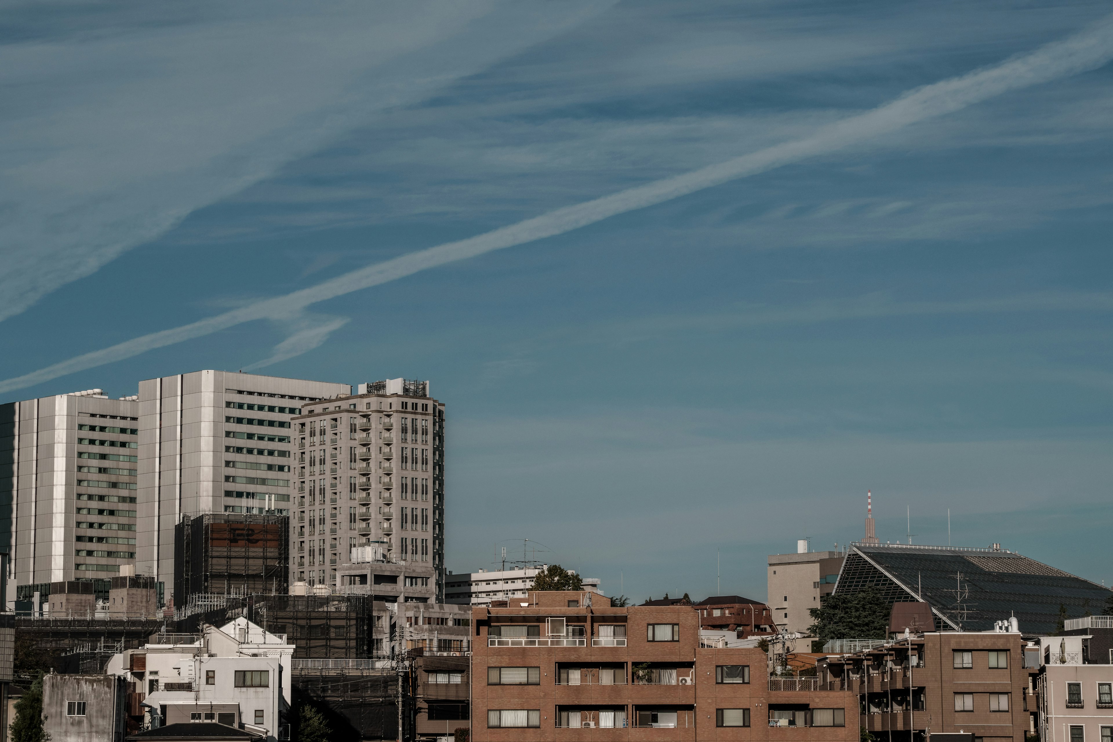 Paisaje urbano con edificios altos y casas de baja altura bajo un cielo azul con nubes en rayas