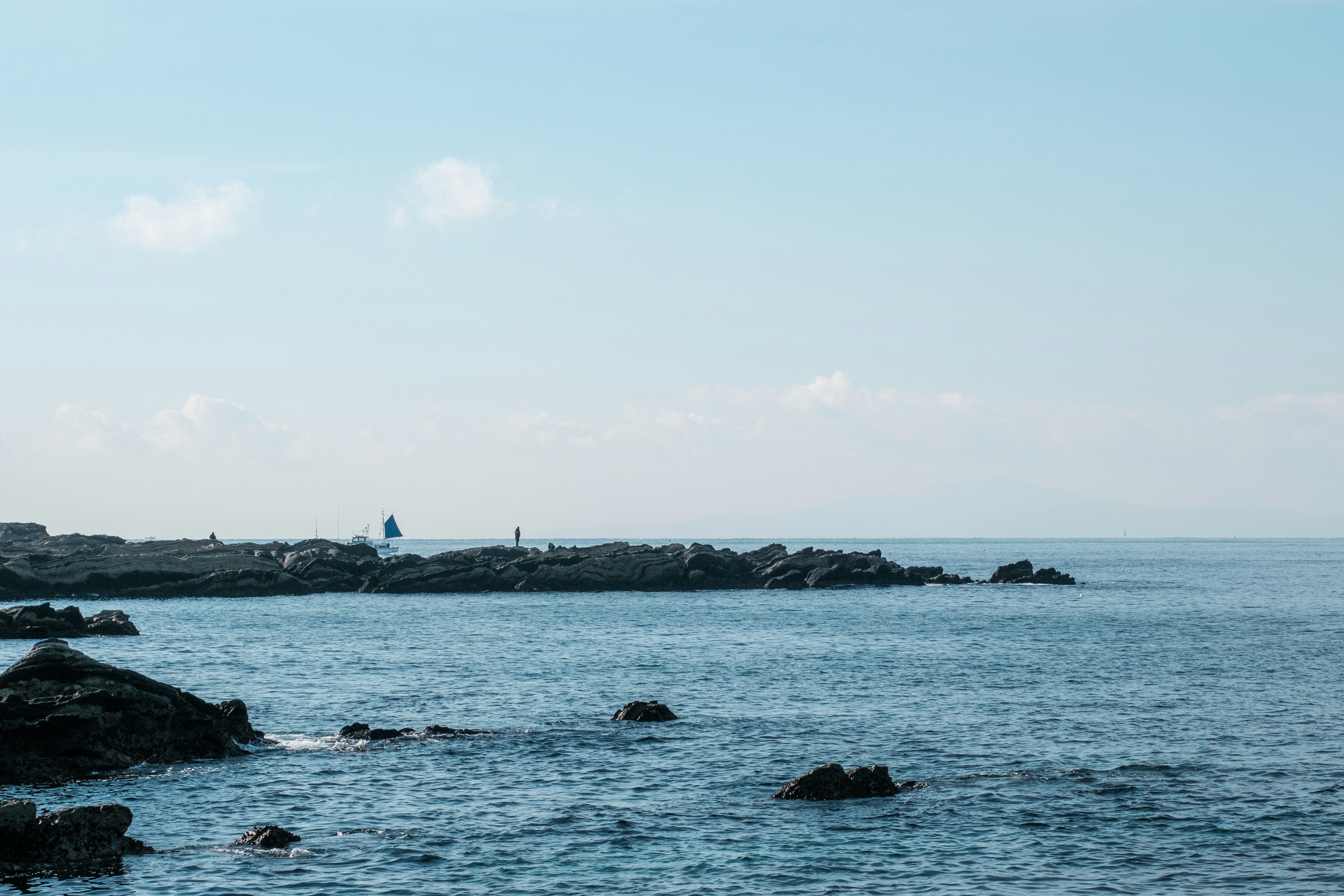 ทิวทัศน์ชายฝั่งที่มีท้องฟ้าสีฟ้าและน้ำสงบใกล้ชายหาดหิน