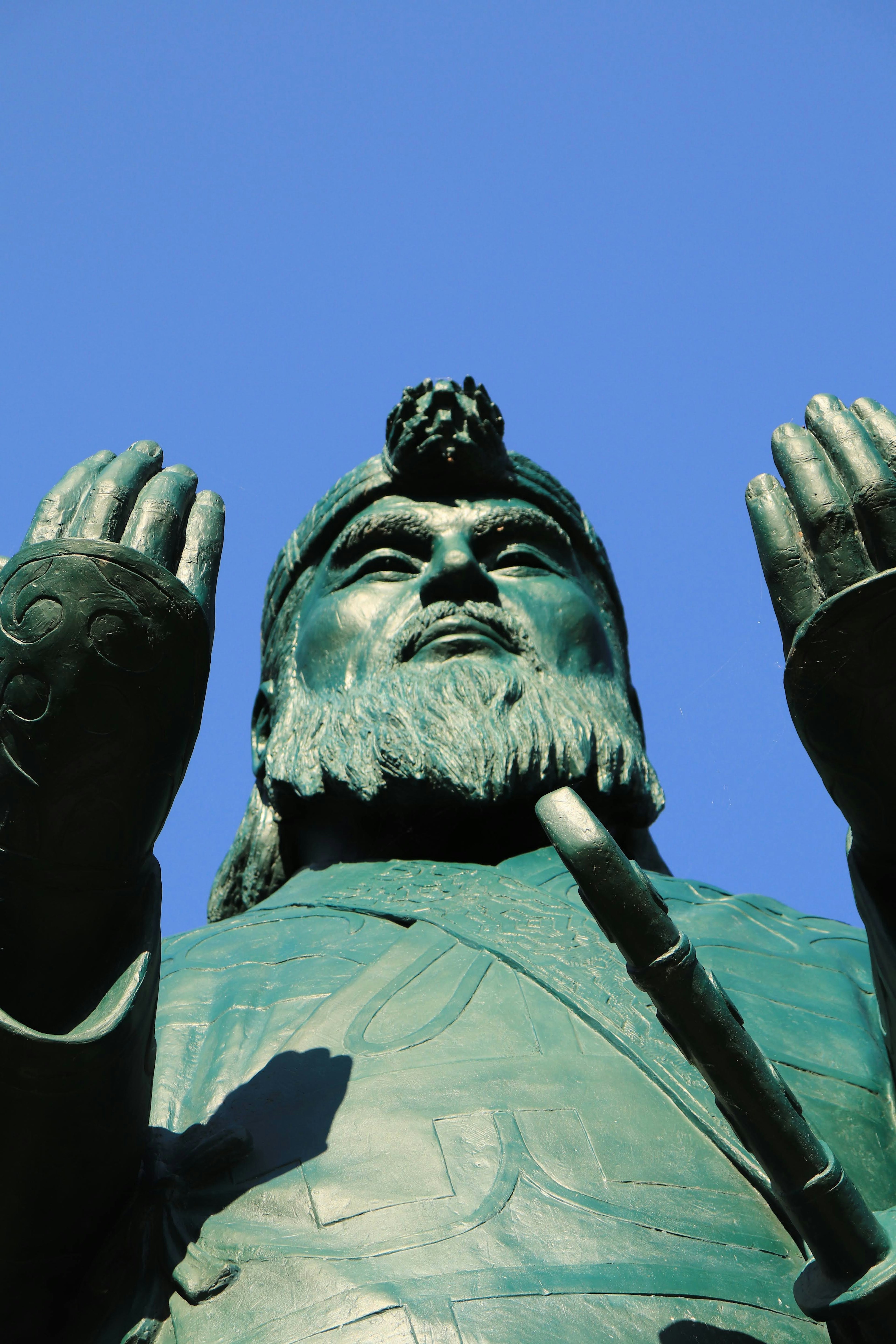 Large bronze statue of a figure with raised hands under a blue sky