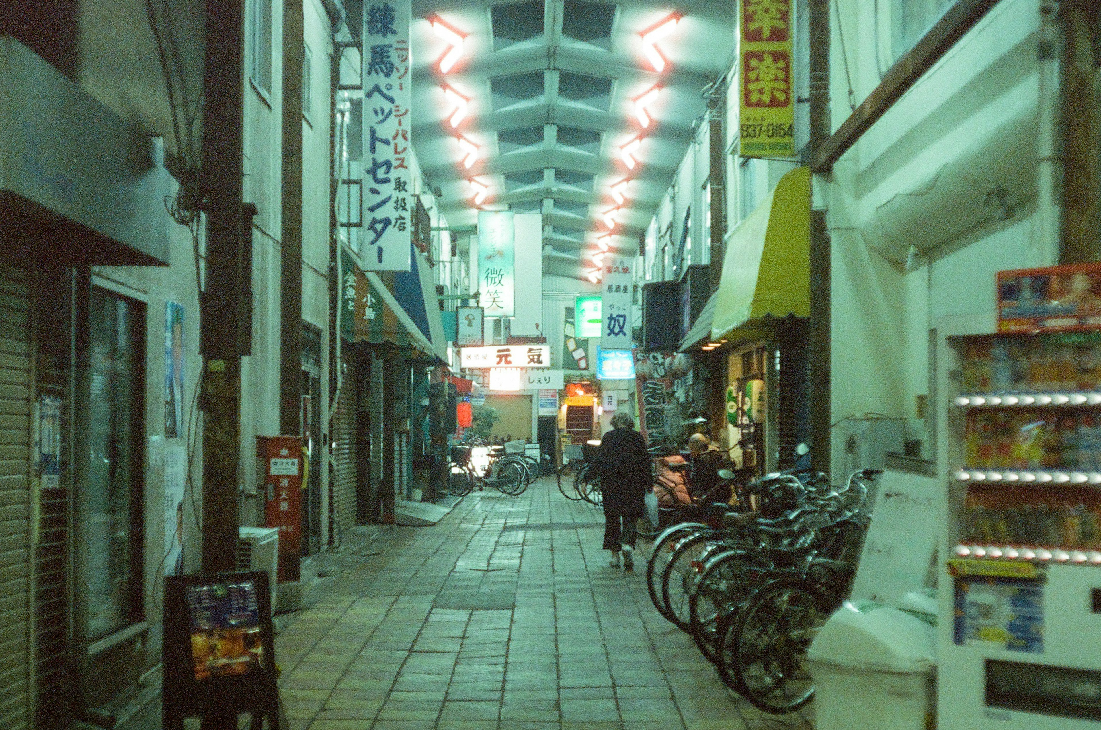 Narrow alley lined with bicycles and shops under neon lights