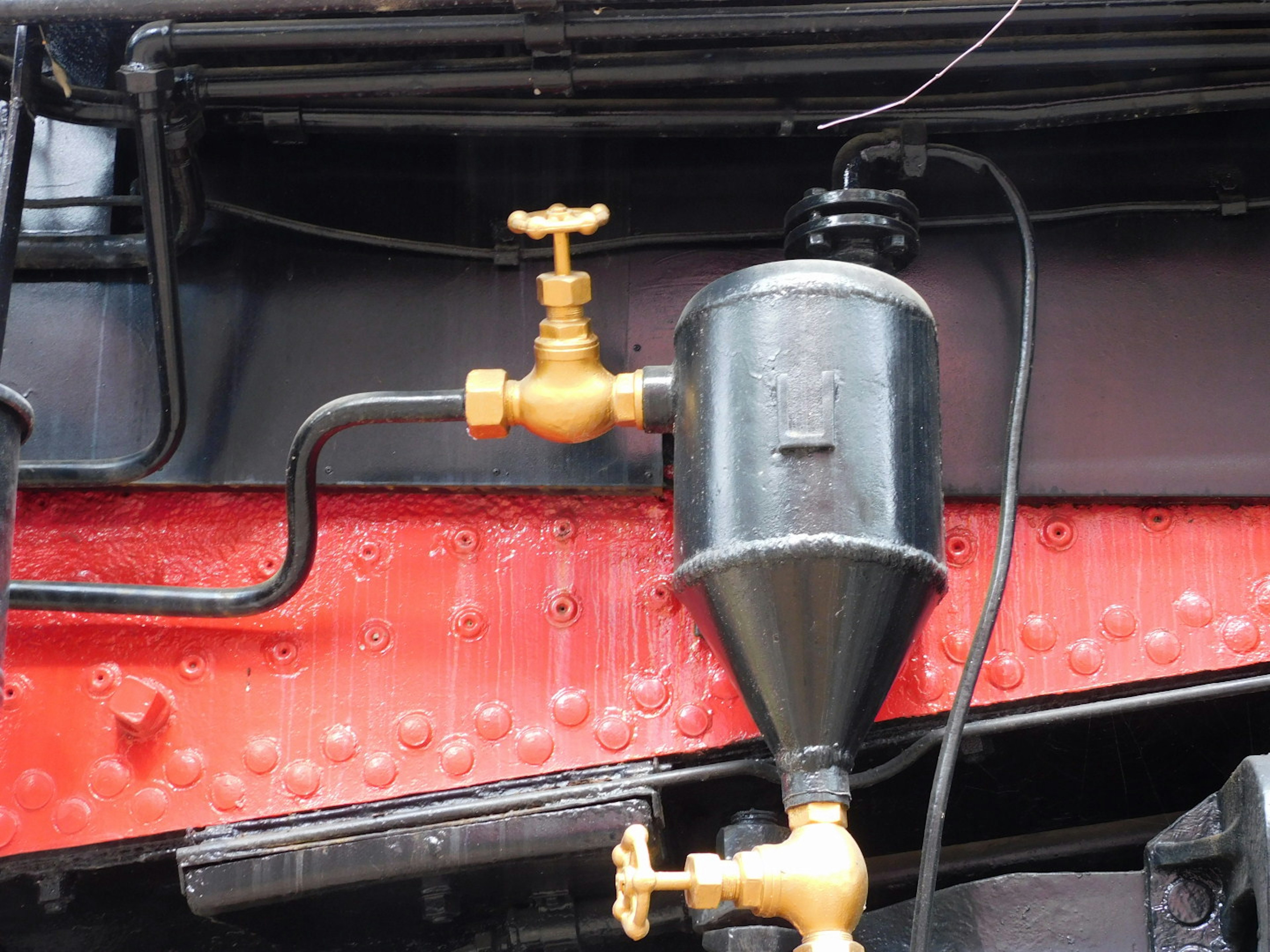 Détail du réservoir hydraulique noir et des tuyauteries d'une locomotive à vapeur