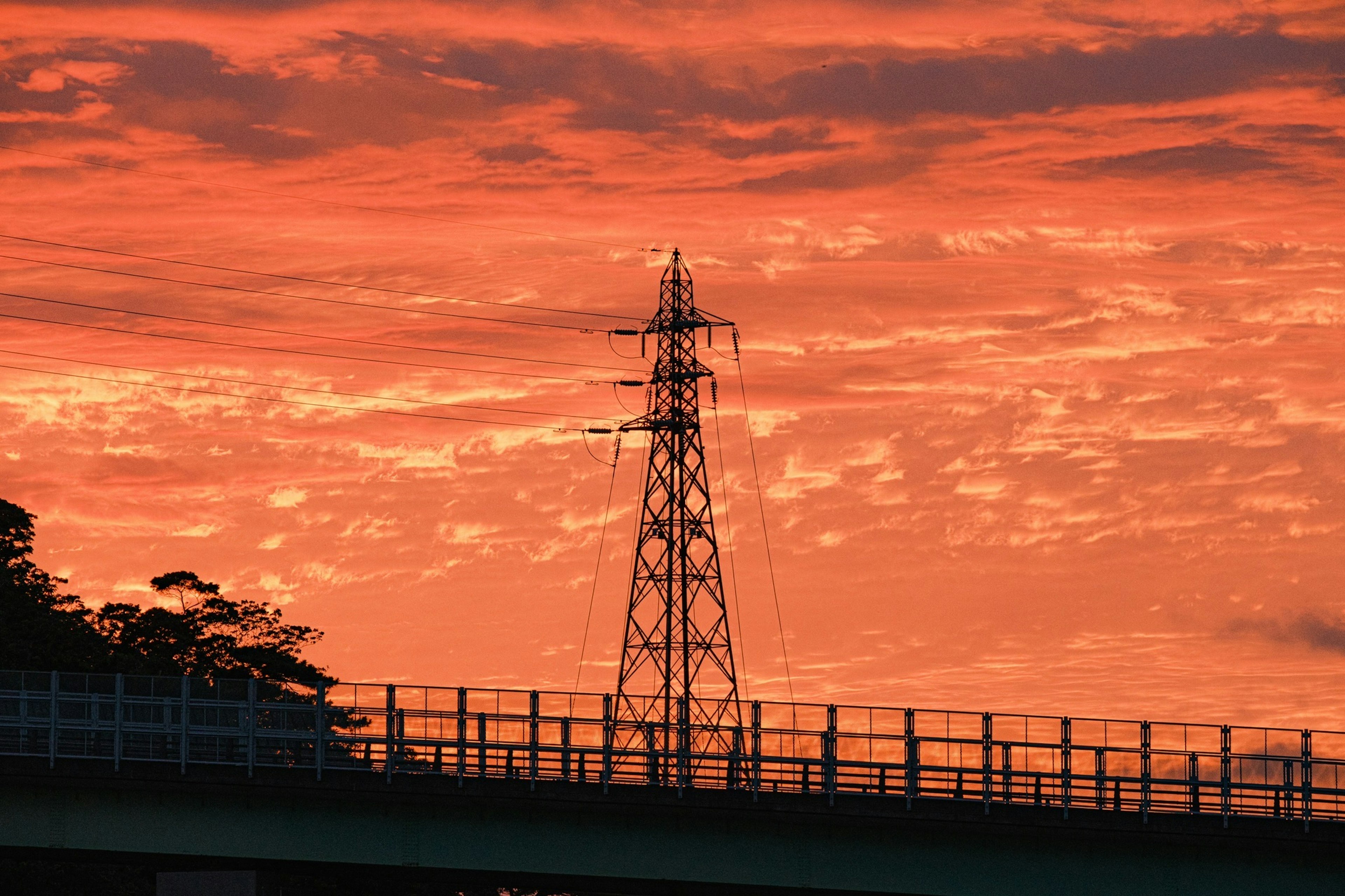 Silueta de una torre de transmisión y un puente contra un cielo al atardecer