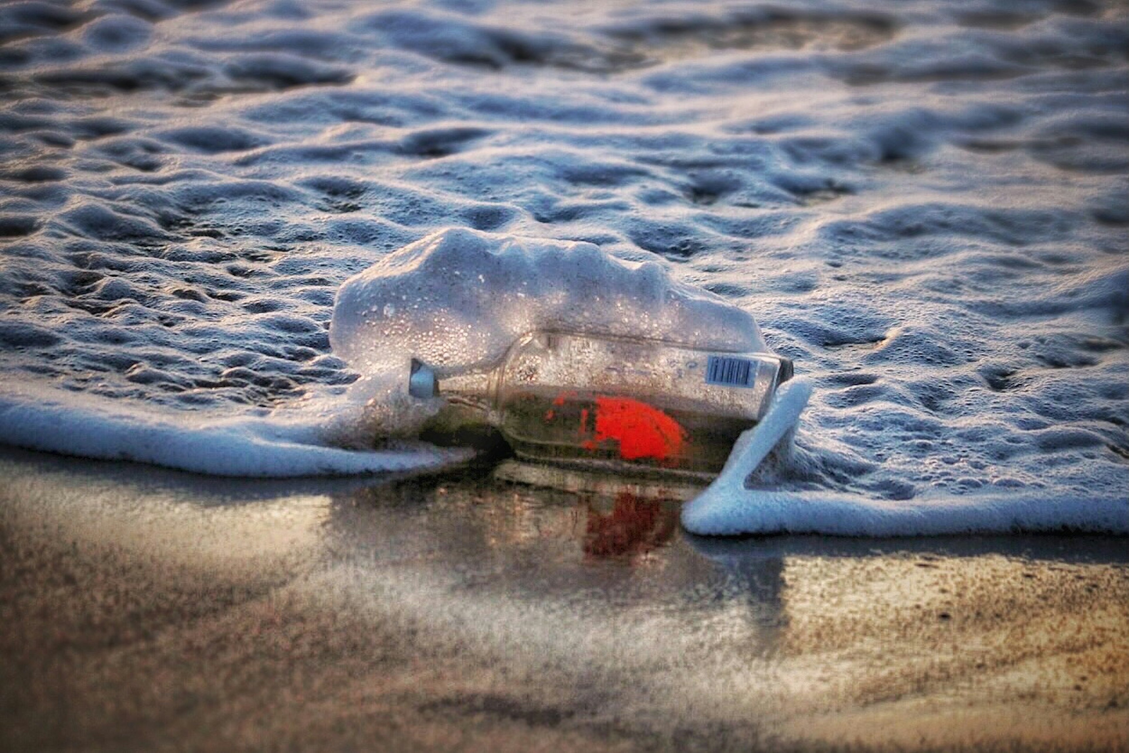 Rote Nachrichtenflasche am Ufer mit Schaum