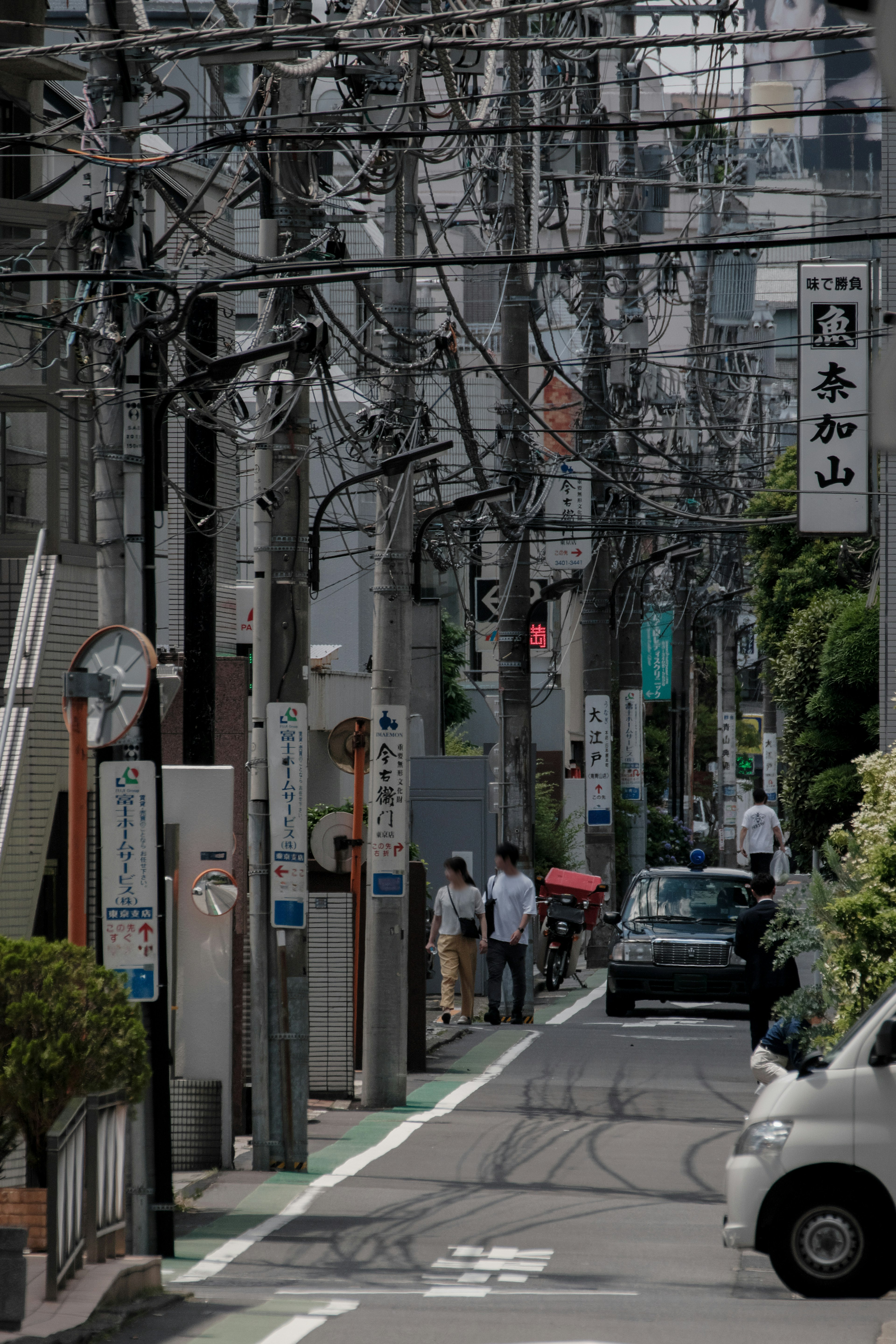 Narrow alley with tangled power lines cars and pedestrians passing by