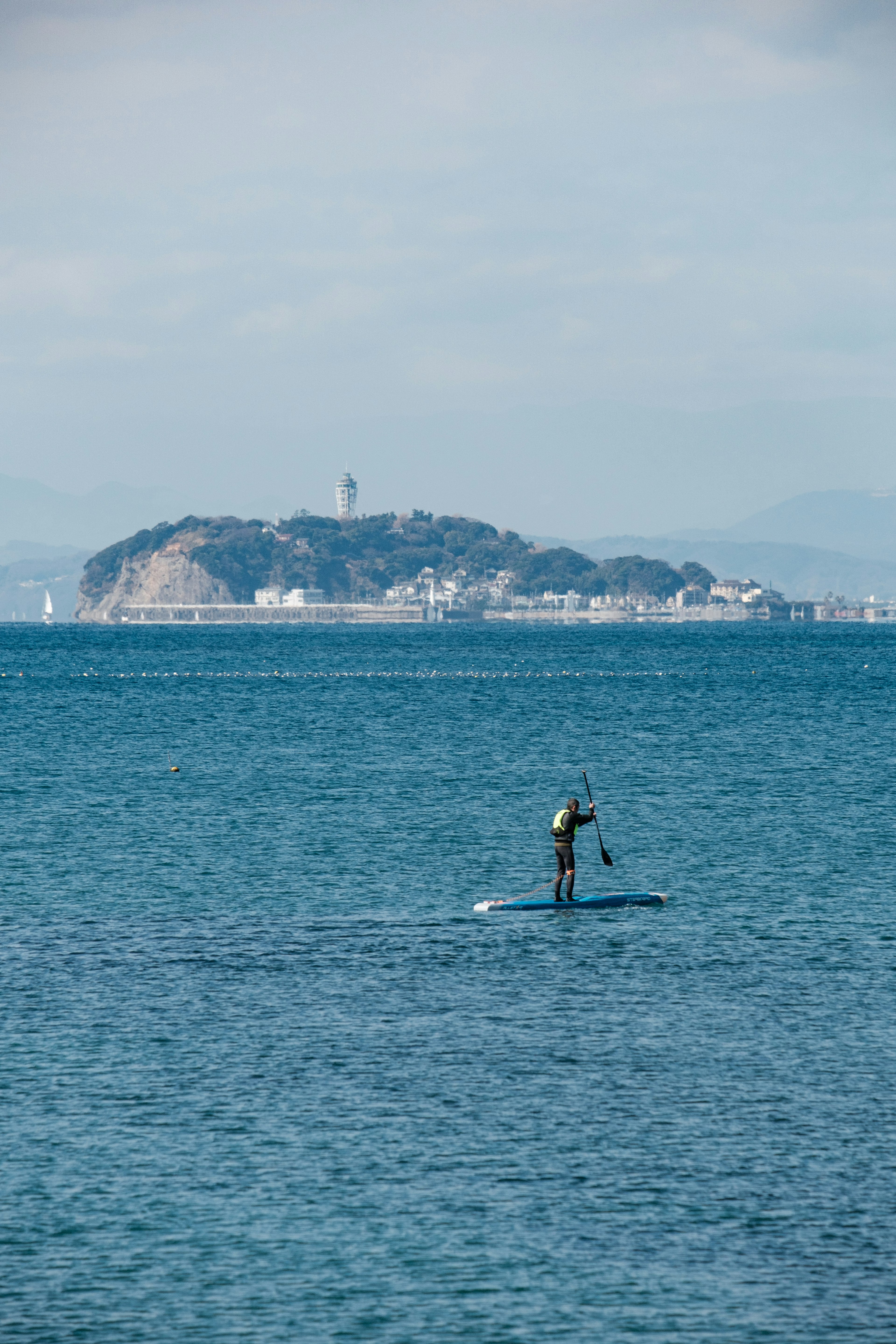 Personne faisant du paddle sur l'eau bleue avec une île au loin